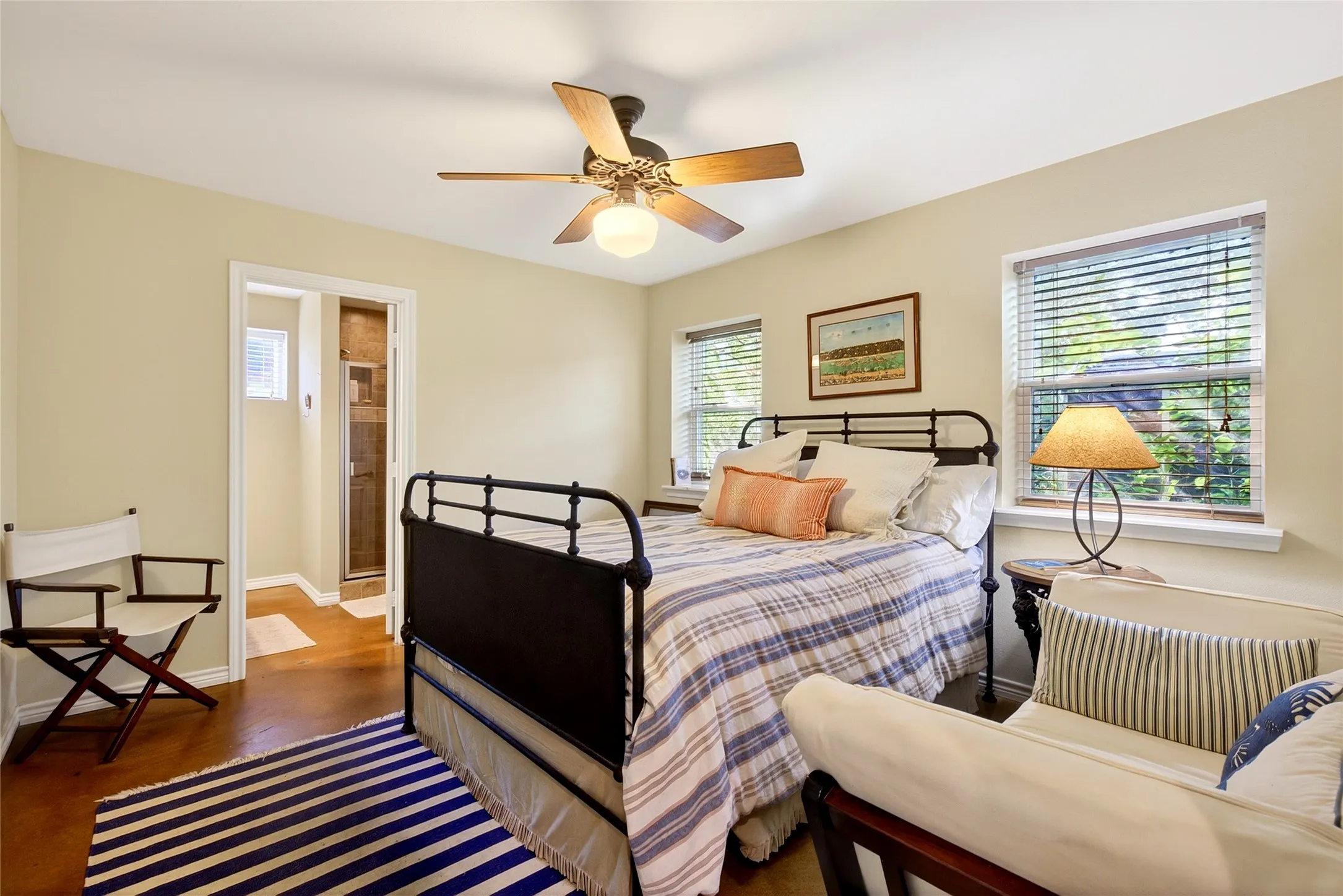 Cabin Primary Bedroom  featuring two windows with blinds, a ceiling fan with integrated lighting, stained concrete flooring, and full bath with a shower including a stackable washer and dryer.