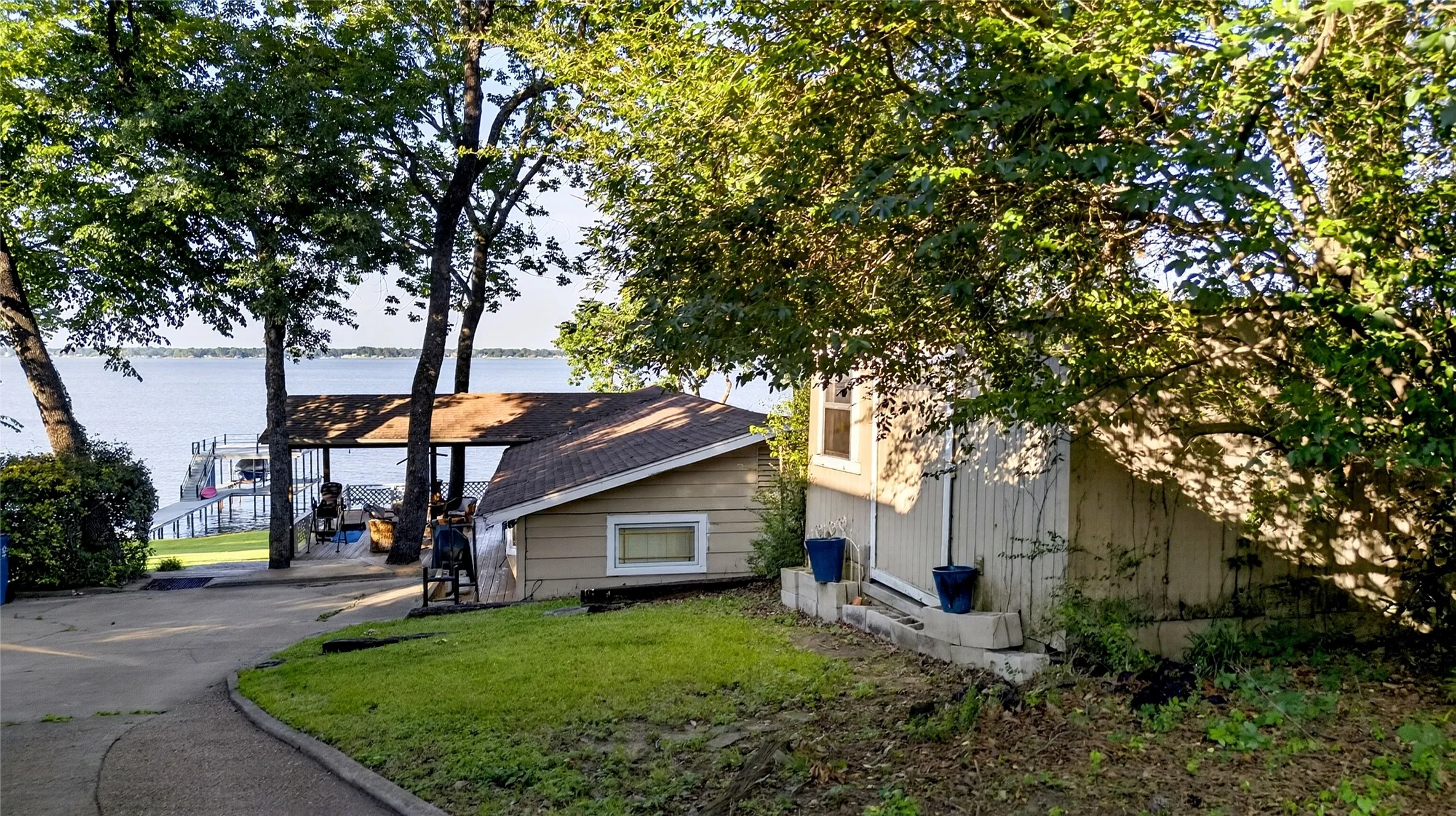 Drive in to the waterfront property featuring main residence, Guest cabin, storage, and a private double deck boat dock with a covered slip, direct water access, mature trees, and a concrete driveway.