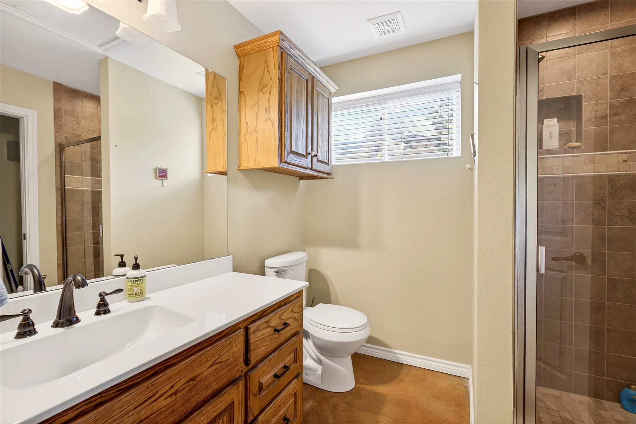 Cabin Primary Full Bathroom featuring a single vanity with wood cabinetry, a white countertop, a dark bronze faucet, with walk-in shower, and a stackable washer and dryer.