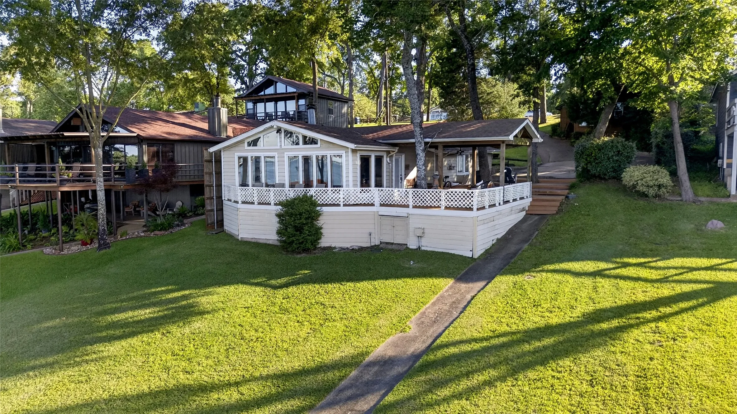 Lakeside view of the waterfront residence featuring a spacious deck with white lattice railings, and a covered patio.