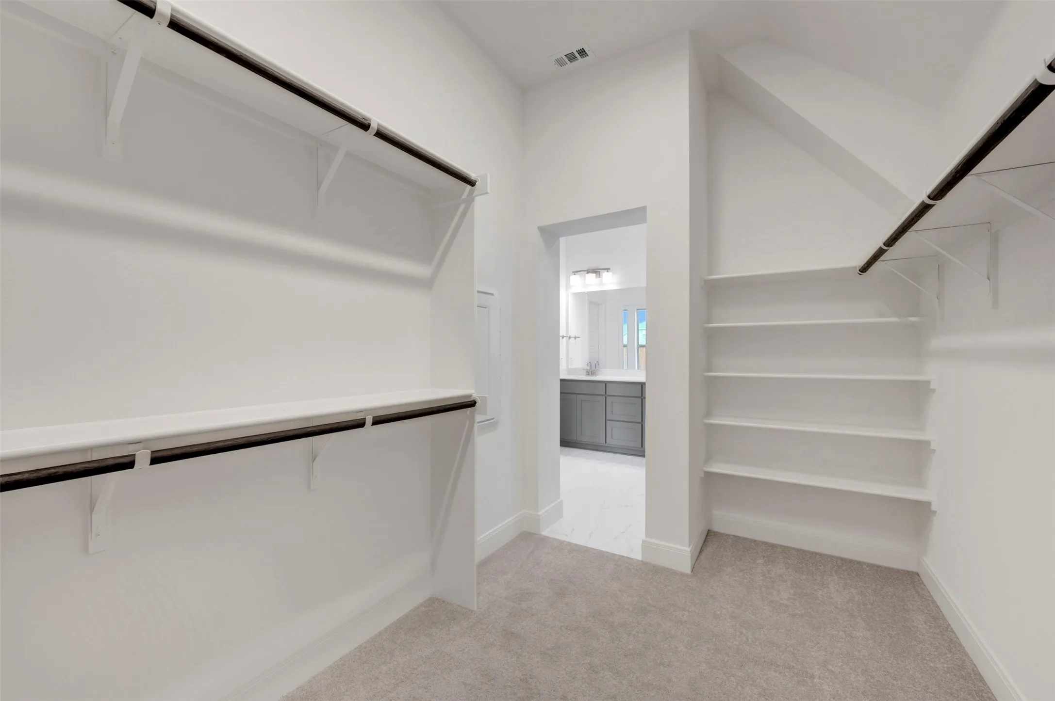 Walk-in closet with carpet flooring, white shelving, and hanging rods