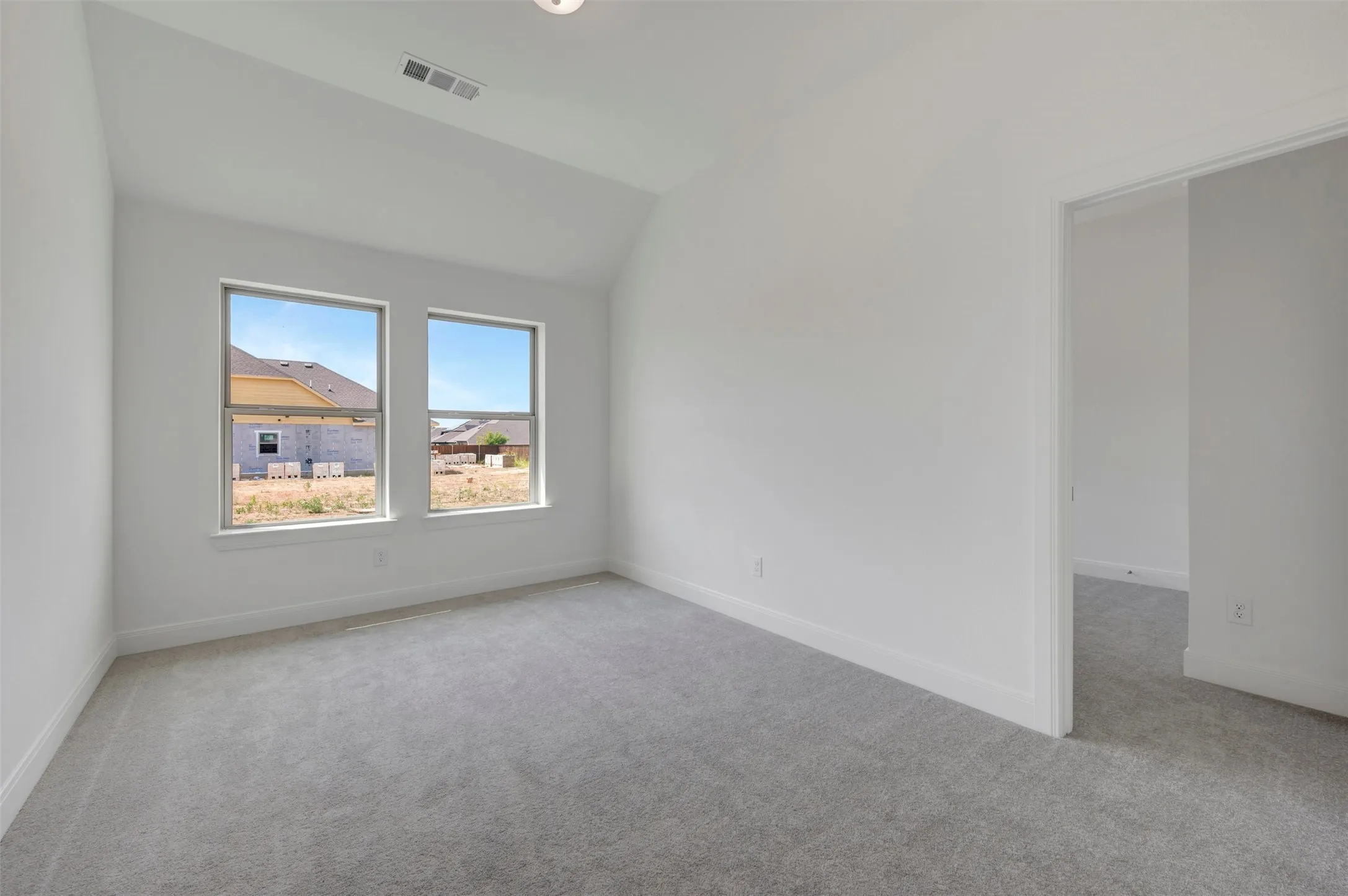 White-painted interior with vaulted ceiling, light gray carpeting, and two large windows