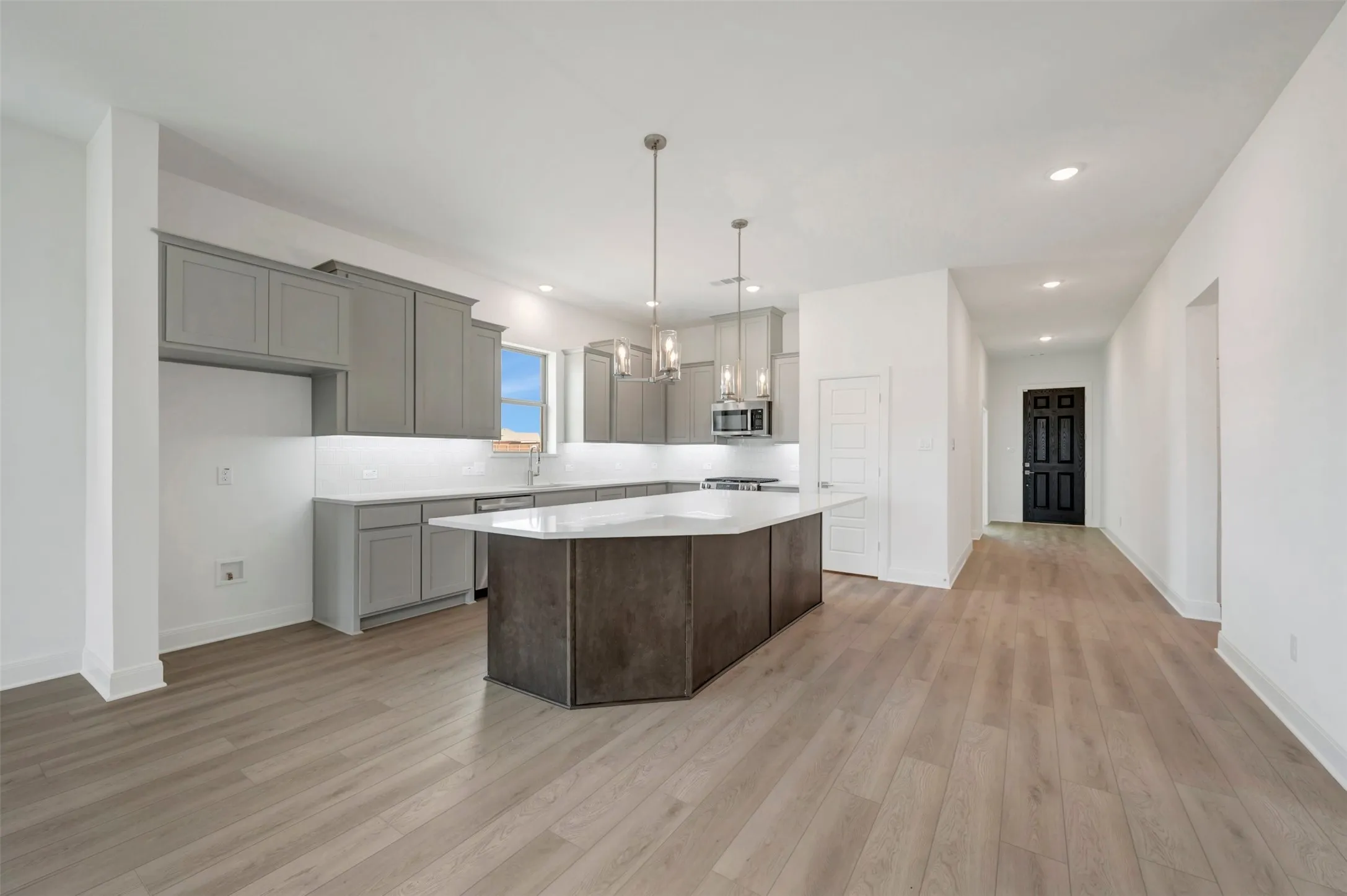 Open-concept kitchen featuring an island with a white countertop, gray cabinetry, stainless steel appliances, and wood-finish flooring