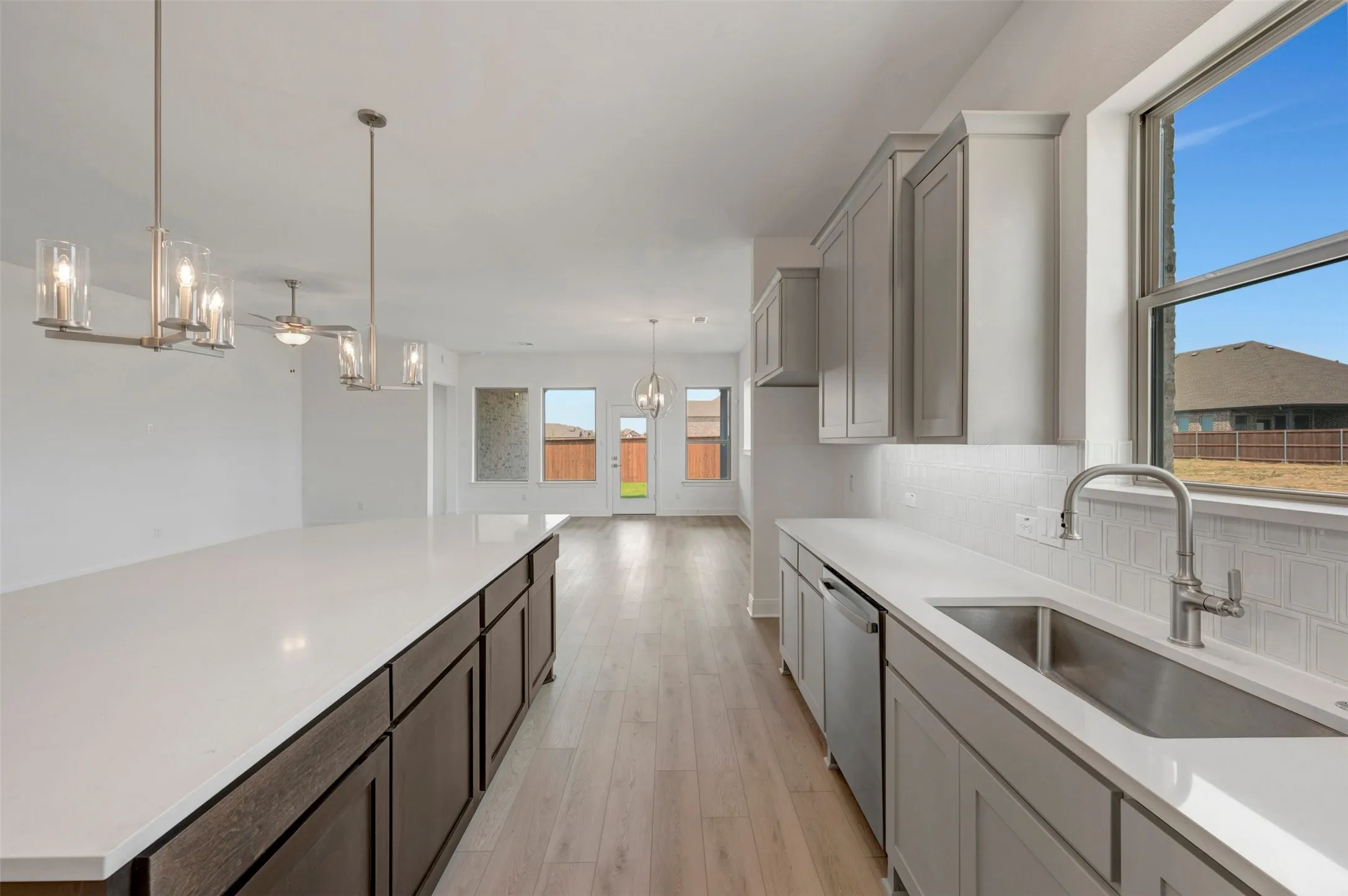 Open-concept kitchen featuring an expansive island with white countertop, sleek gray cabinetry, stainless steel sink, and wood-finish flooring