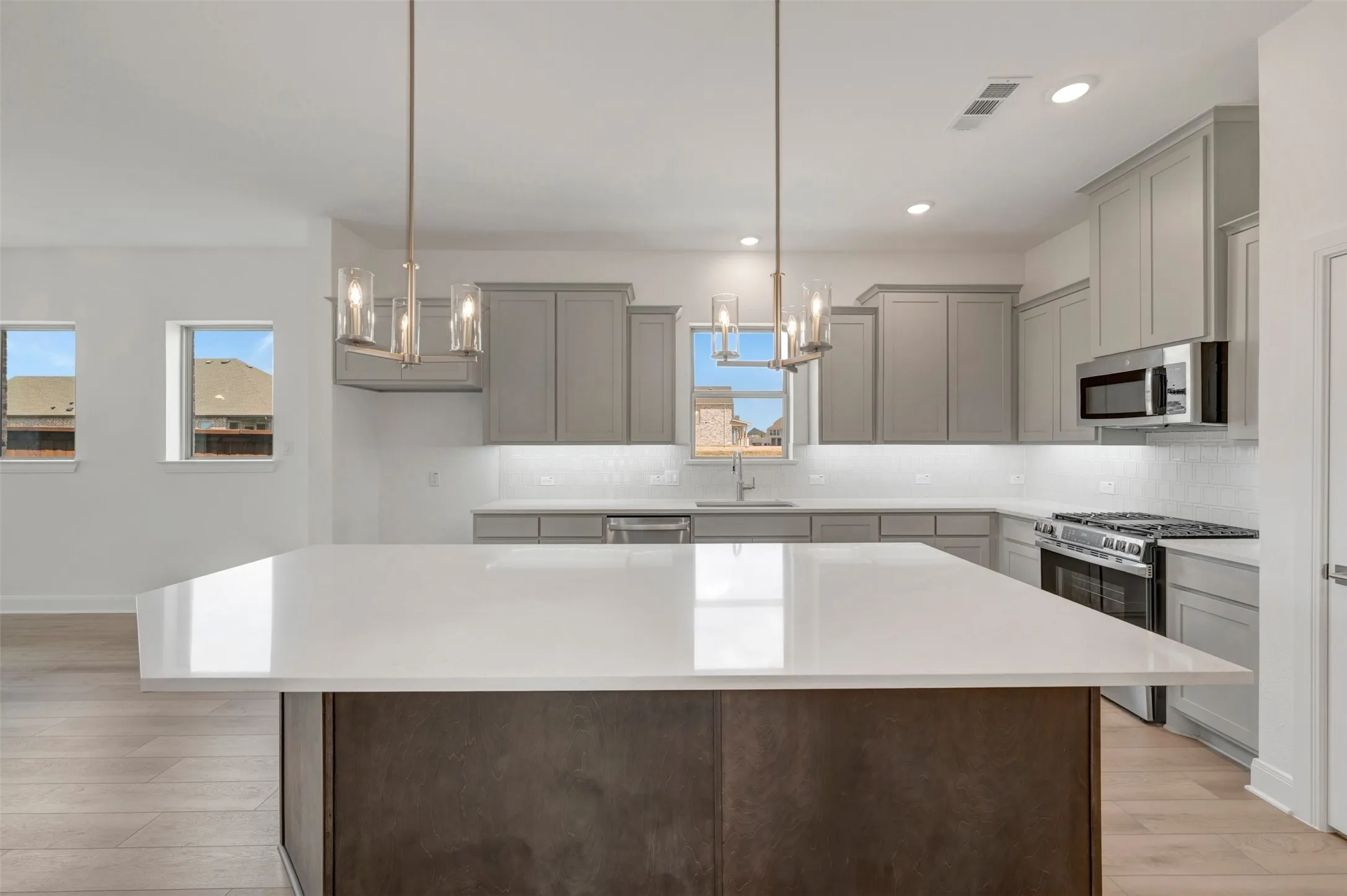 Expansive kitchen island with a bright countertop, gray cabinetry, stainless steel appliances, and wood-finish flooring