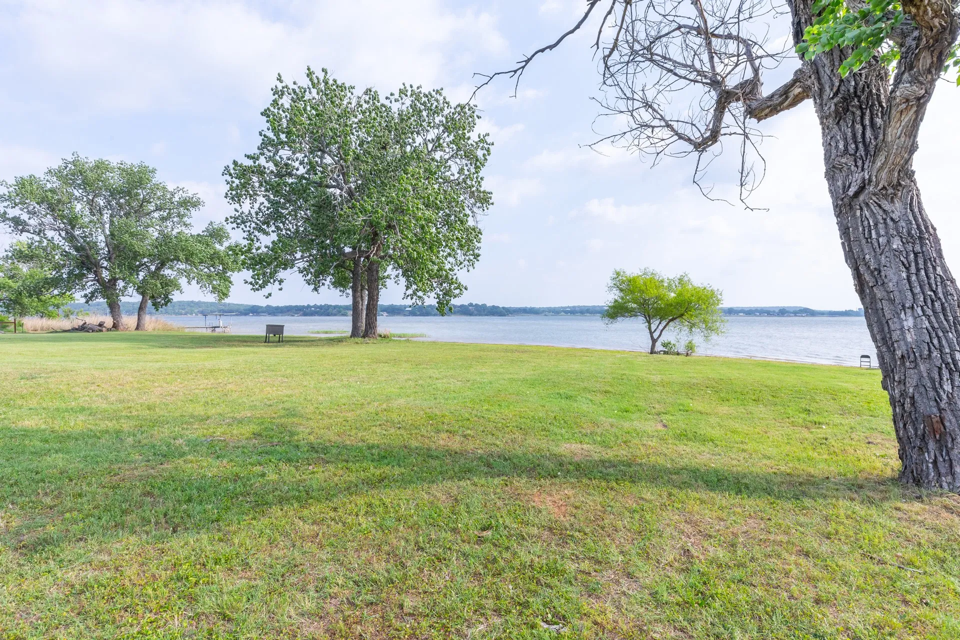 Expansive green lawn with mature trees, bordered by a body of water