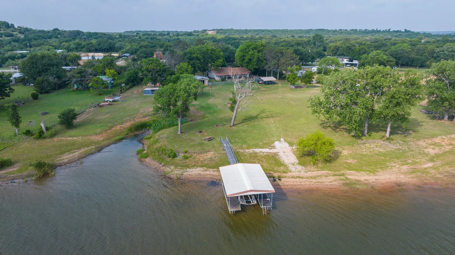 Waterfront property featuring a private boat dock with a covered slip, expansive green lawn, mature trees, and a residential structure