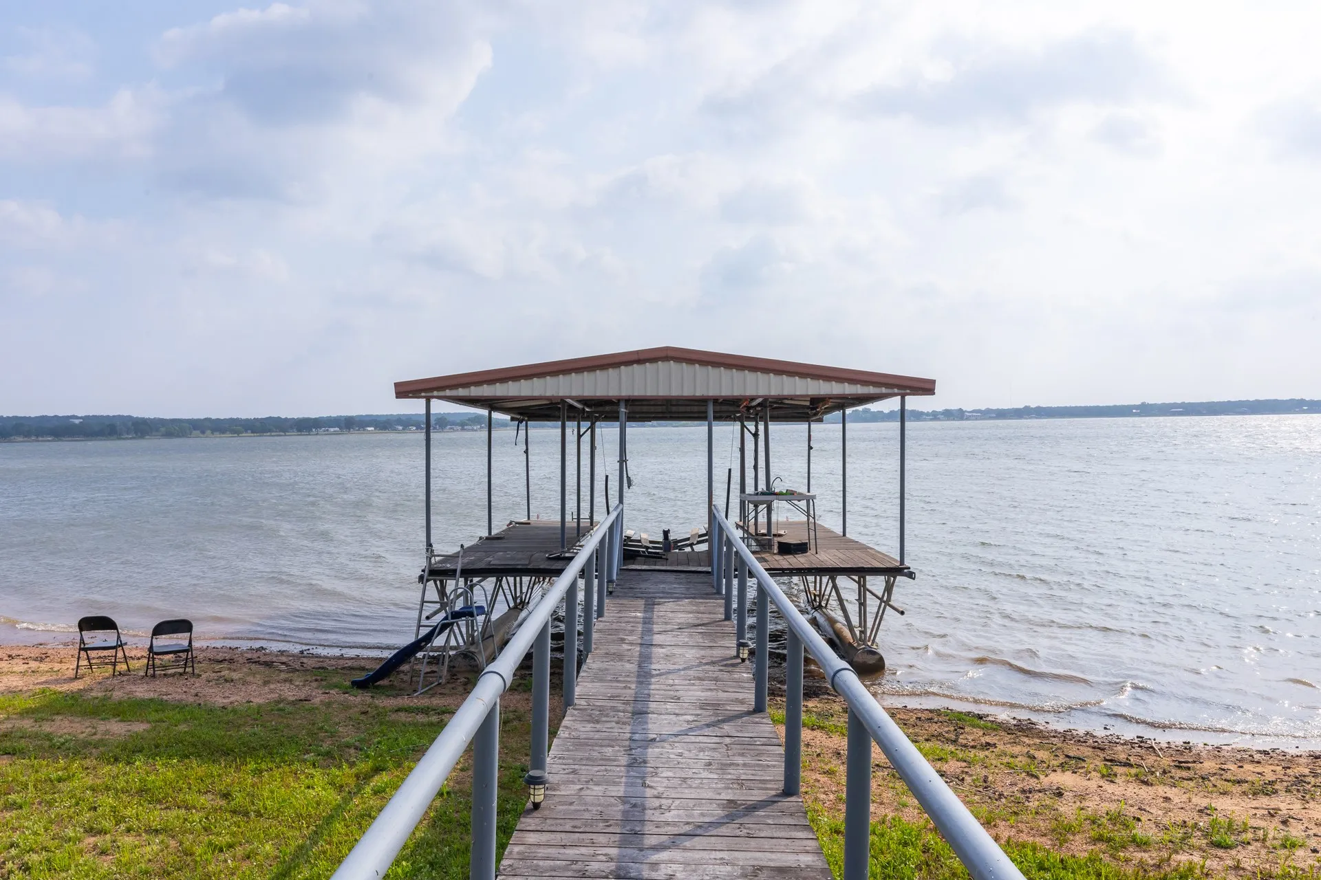 Private boat dock featuring a covered slip, wood-finish decking, and metal railings