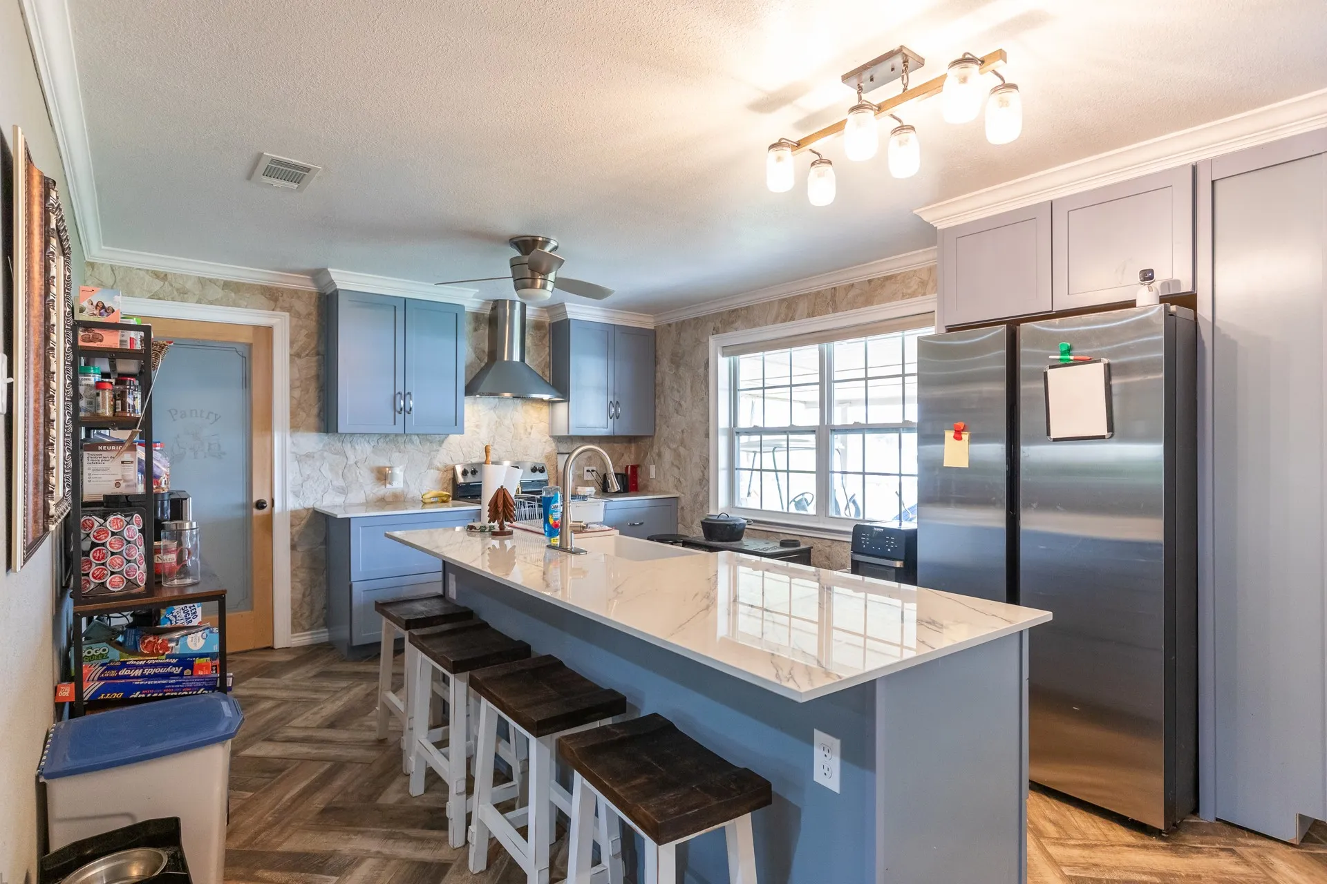 Kitchen featuring a large central island with seating, stainless steel appliances, light blue cabinetry, and wood-finish flooring