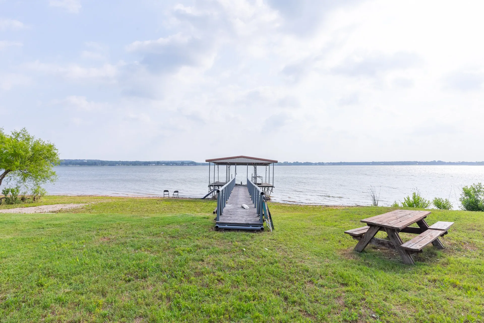 Waterfront property featuring a private covered boat dock, direct water access, a sandy shoreline, and a substantial grassy area