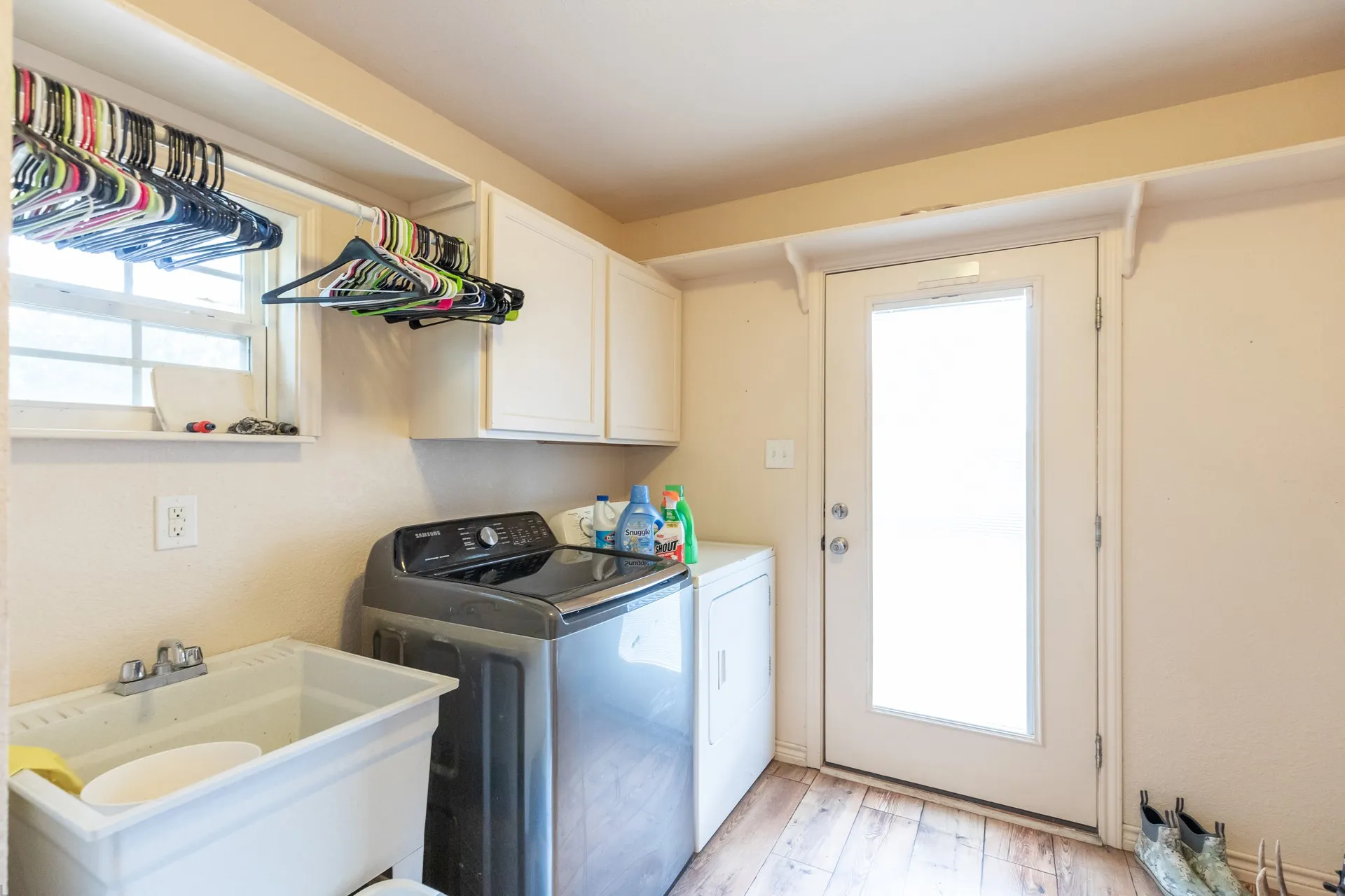 Dedicated laundry space featuring wood-finish flooring, a utility sink, and overhead cabinetry