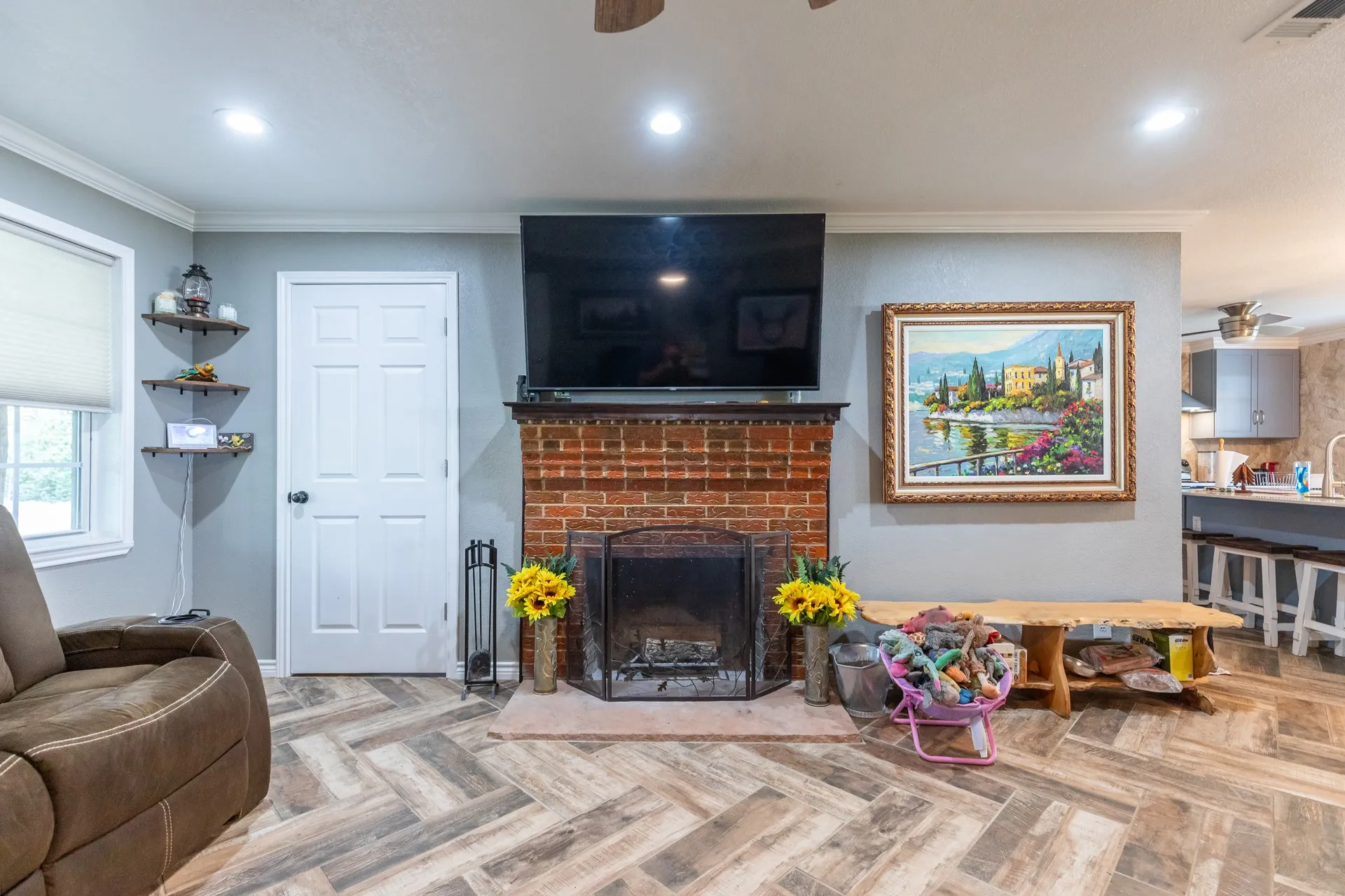 Living area featuring a brick-front fireplace, wood-finish flooring in a herringbone pattern, crown molding, and recessed lighting