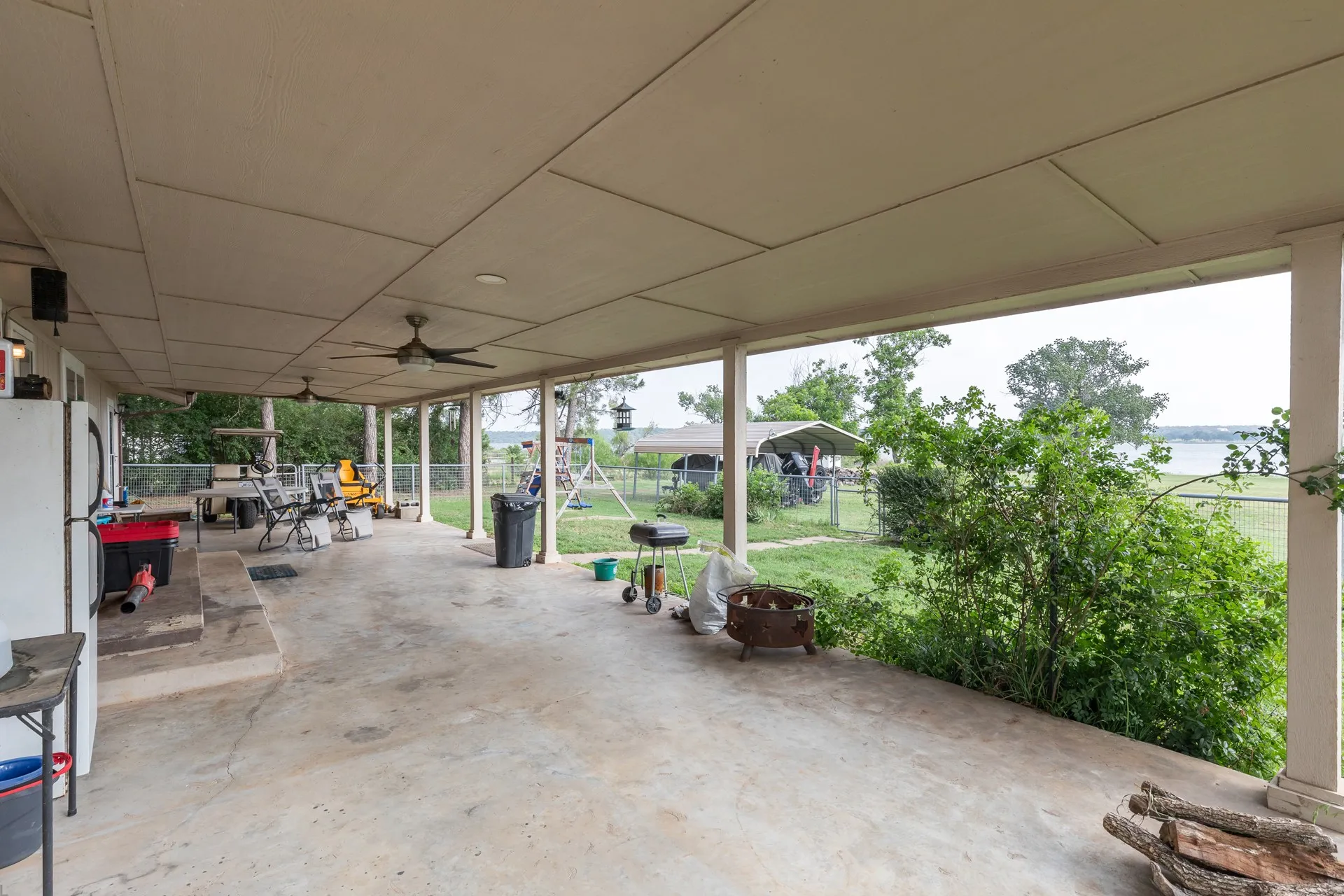 Expansive covered patio featuring concrete flooring, multiple ceiling fans, and a distant water body