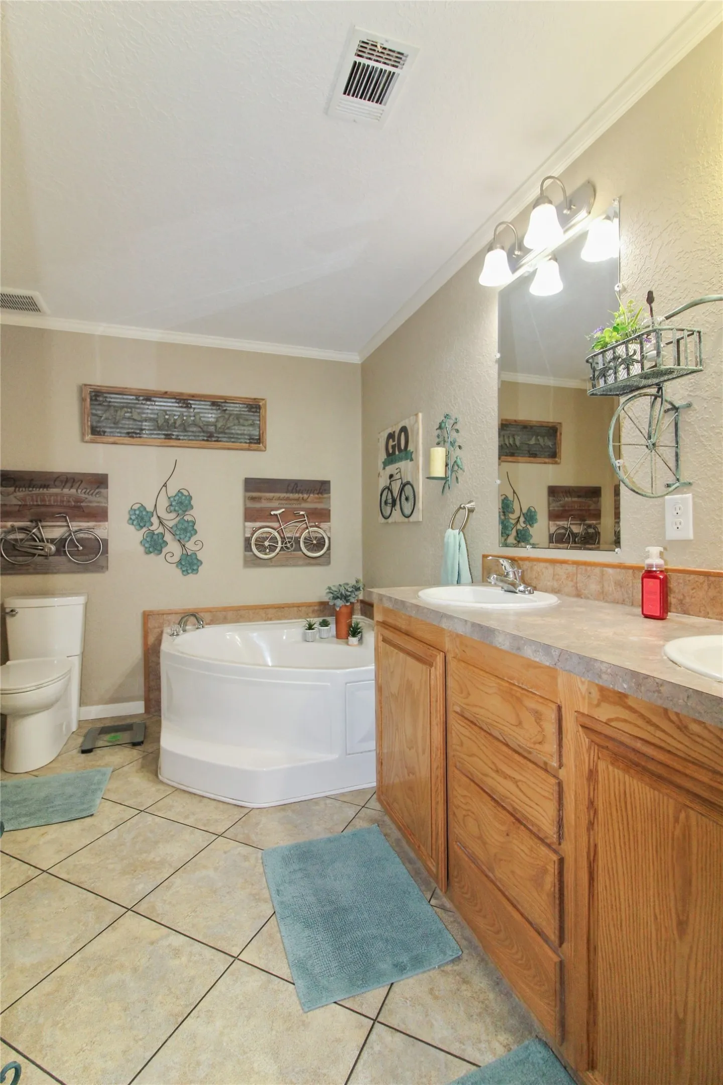Bathroom featuring a corner soaking tub with deck-mounted fixtures, dual vanity with wood-finish cabinetry, ceramic tile flooring, and a standard toilet