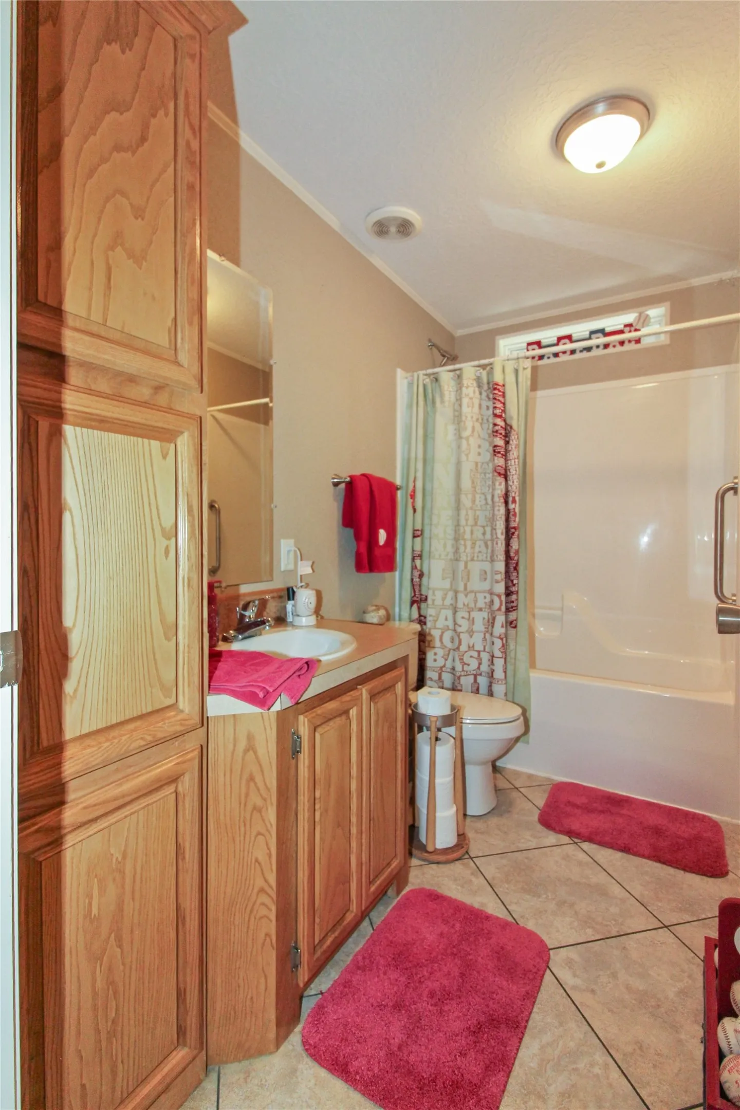 Bathroom featuring a built-in wood-finish cabinetry, a single vanity with an integrated sink, a commode, and a tub/shower combination