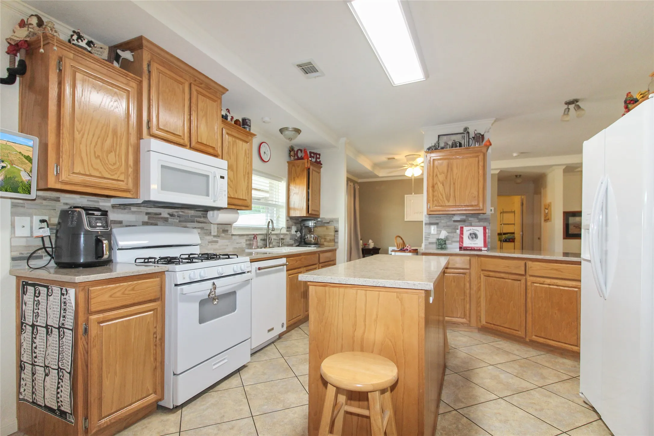Kitchen featuring light wood-finish cabinetry, light-toned stone-finish countertops, a tile backsplash, white appliances, and tile flooring