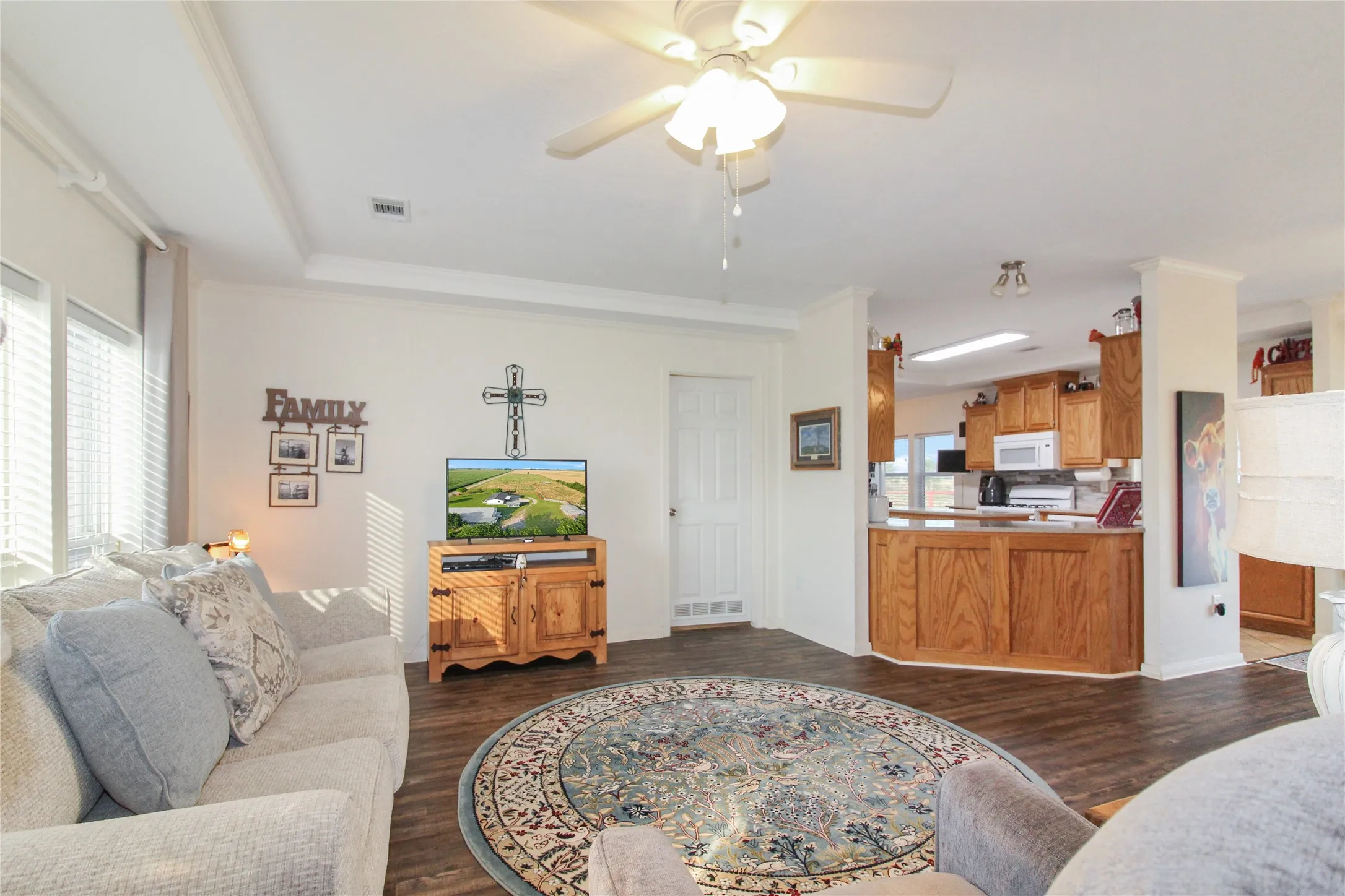 Spacious living area featuring wood-finish flooring, ample natural light from multiple windows, and a ceiling fan