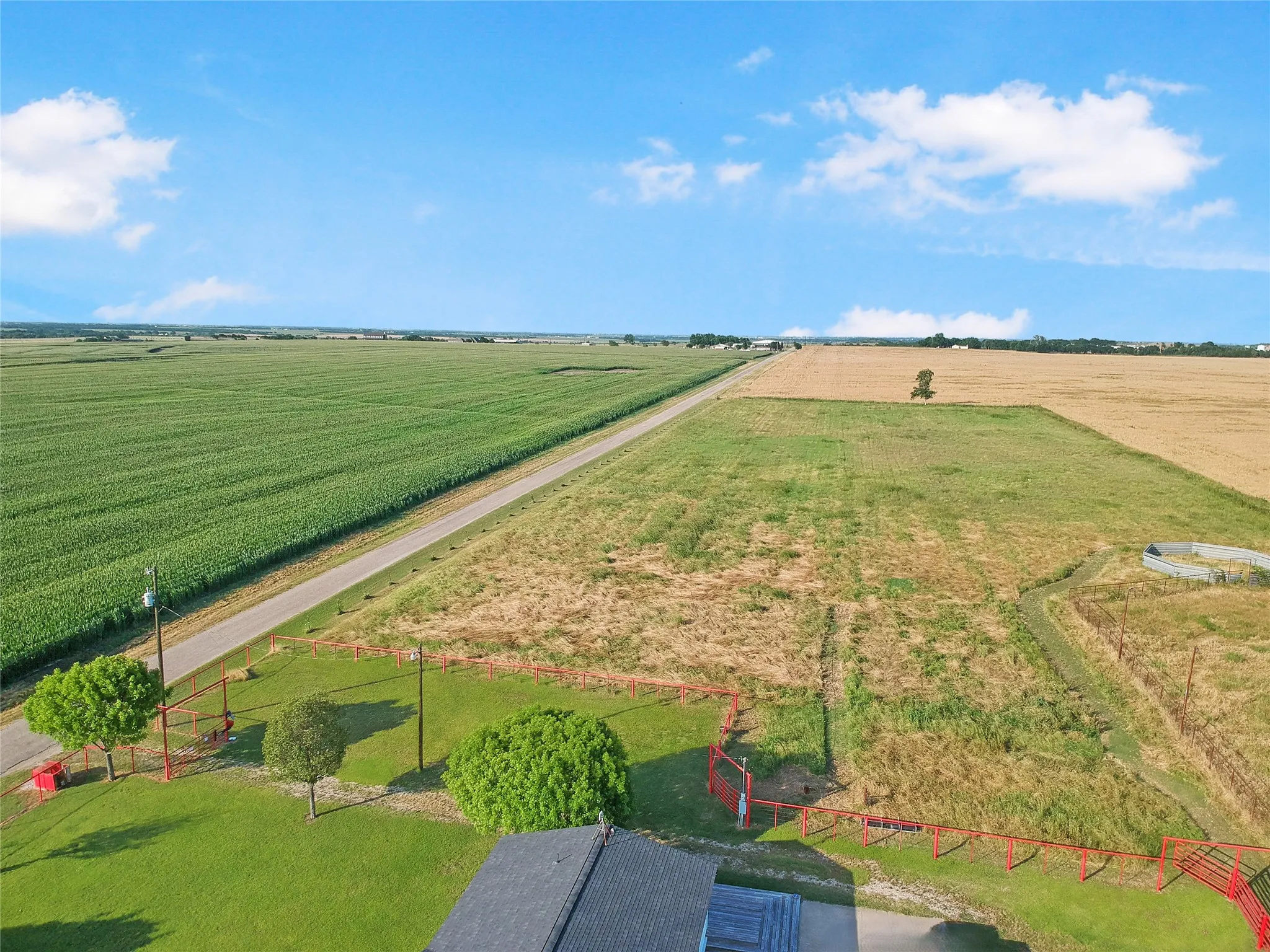 Expansive property featuring a paved road, fenced perimeter, and mature trees, surrounded by agricultural fields