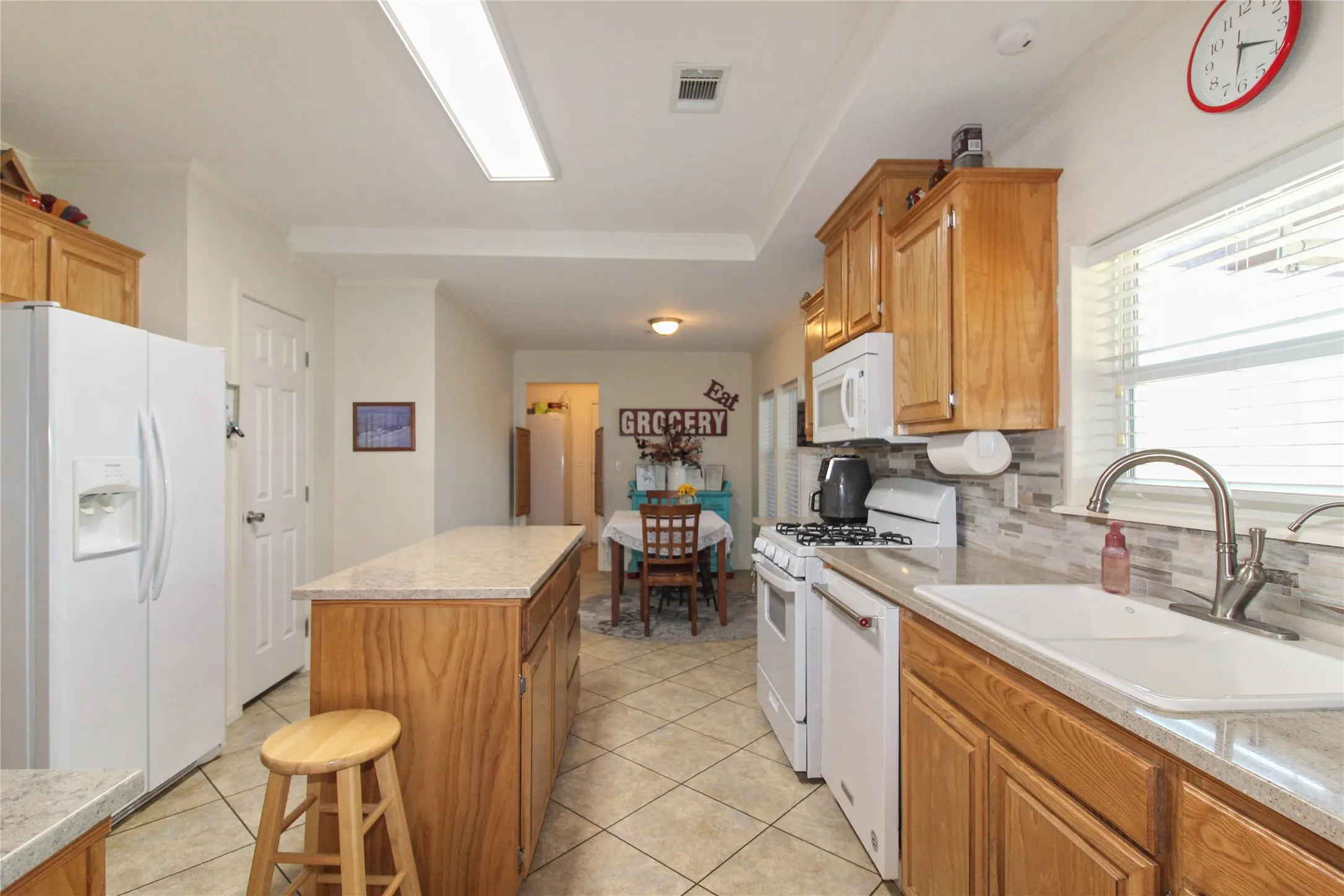Kitchen featuring wood cabinetry, light-toned countertops, a tile backsplash, and a large sink with a gooseneck faucet