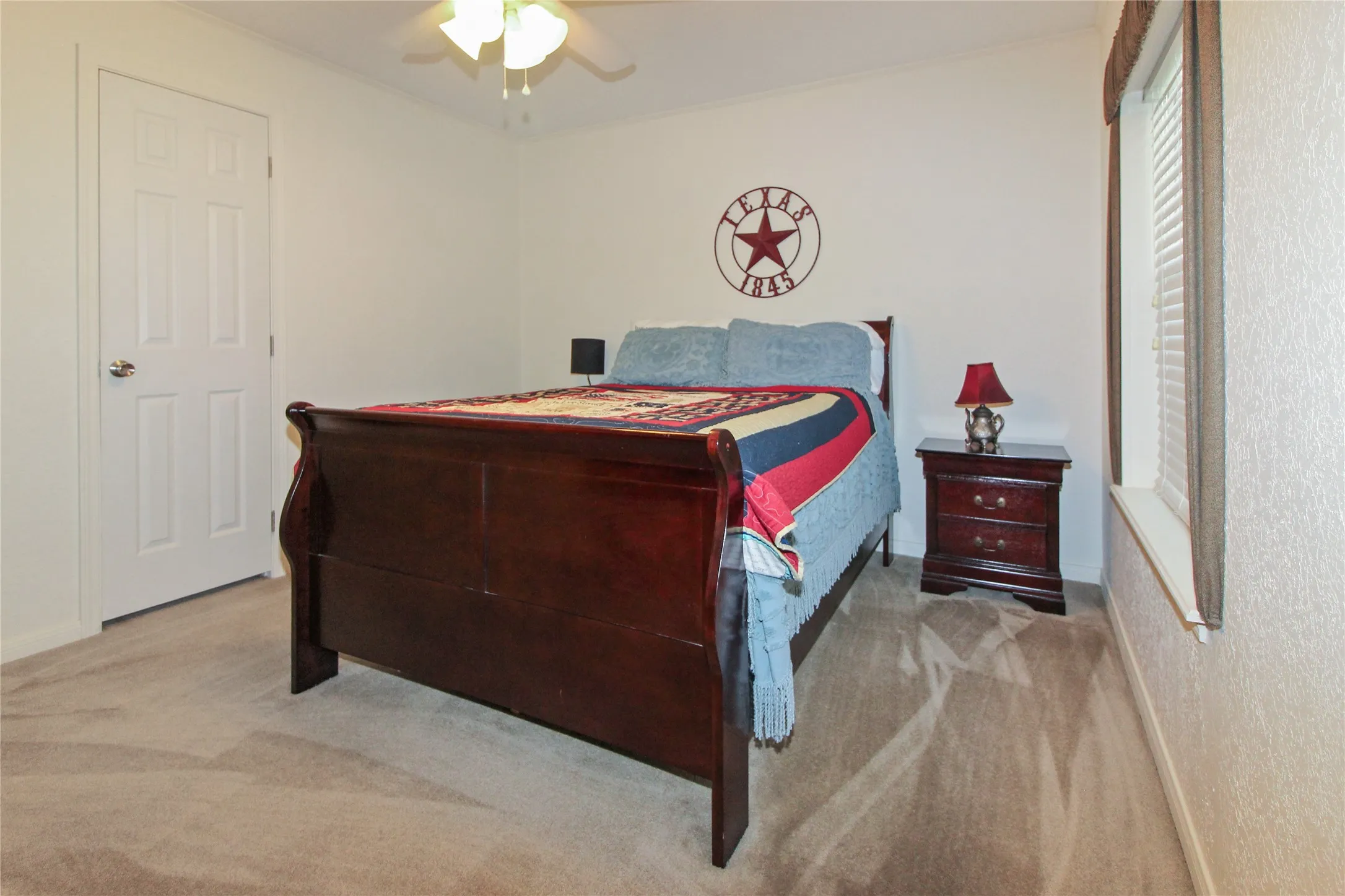 Carpeted bedroom featuring a ceiling fan, a white paneled door, and a window with blinds