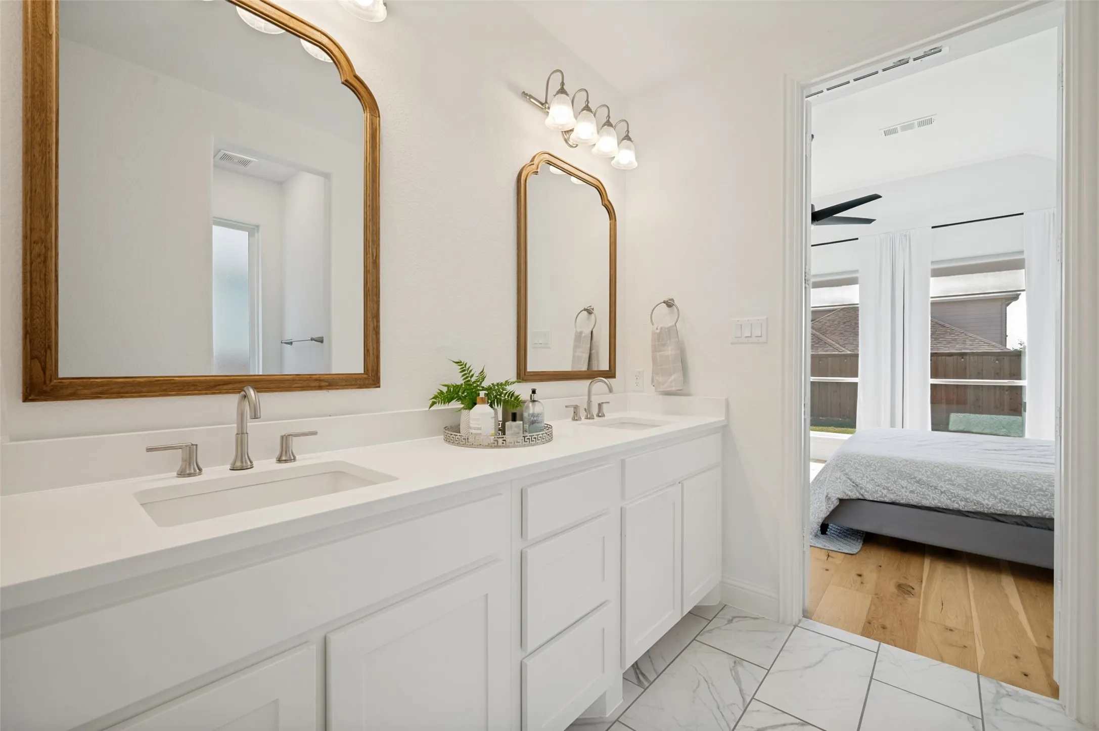 Modern white counters and cabinets create a visual contrast to the light wood accent mirrors giving this primary bathroom a soft, spa like atmosphere