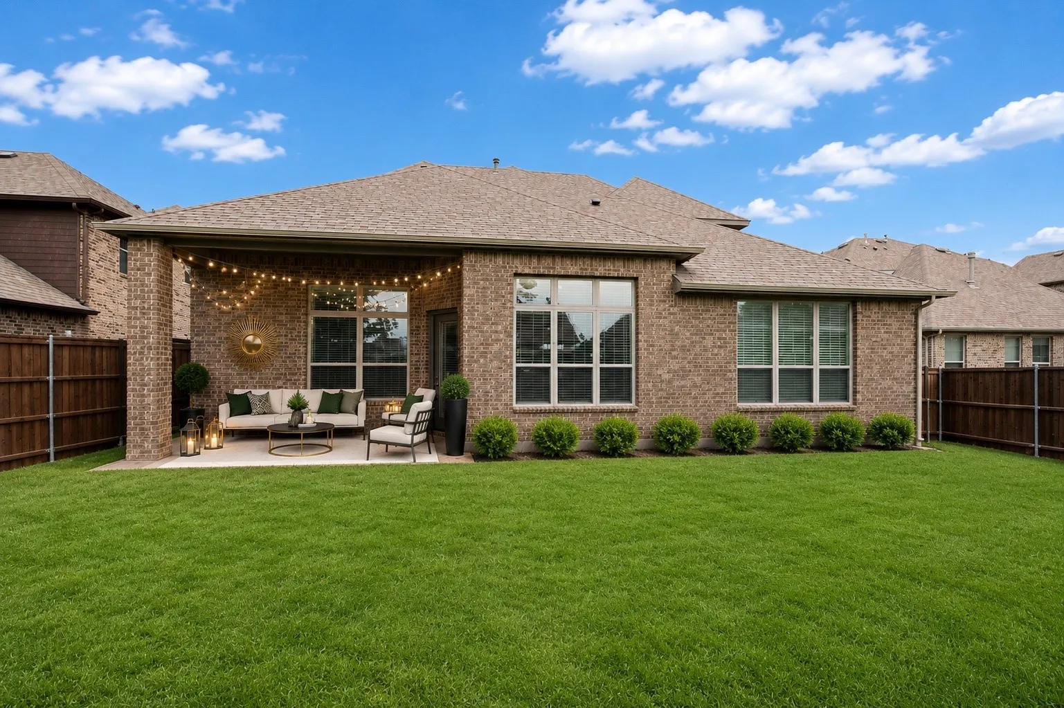 Expansive backyard featuring a manicured lawn, a covered patio, brick exterior, and multiple windows