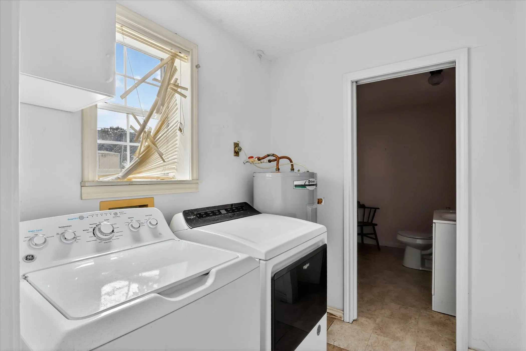 Laundry area featuring white walls, a window, and a water heater and half bath