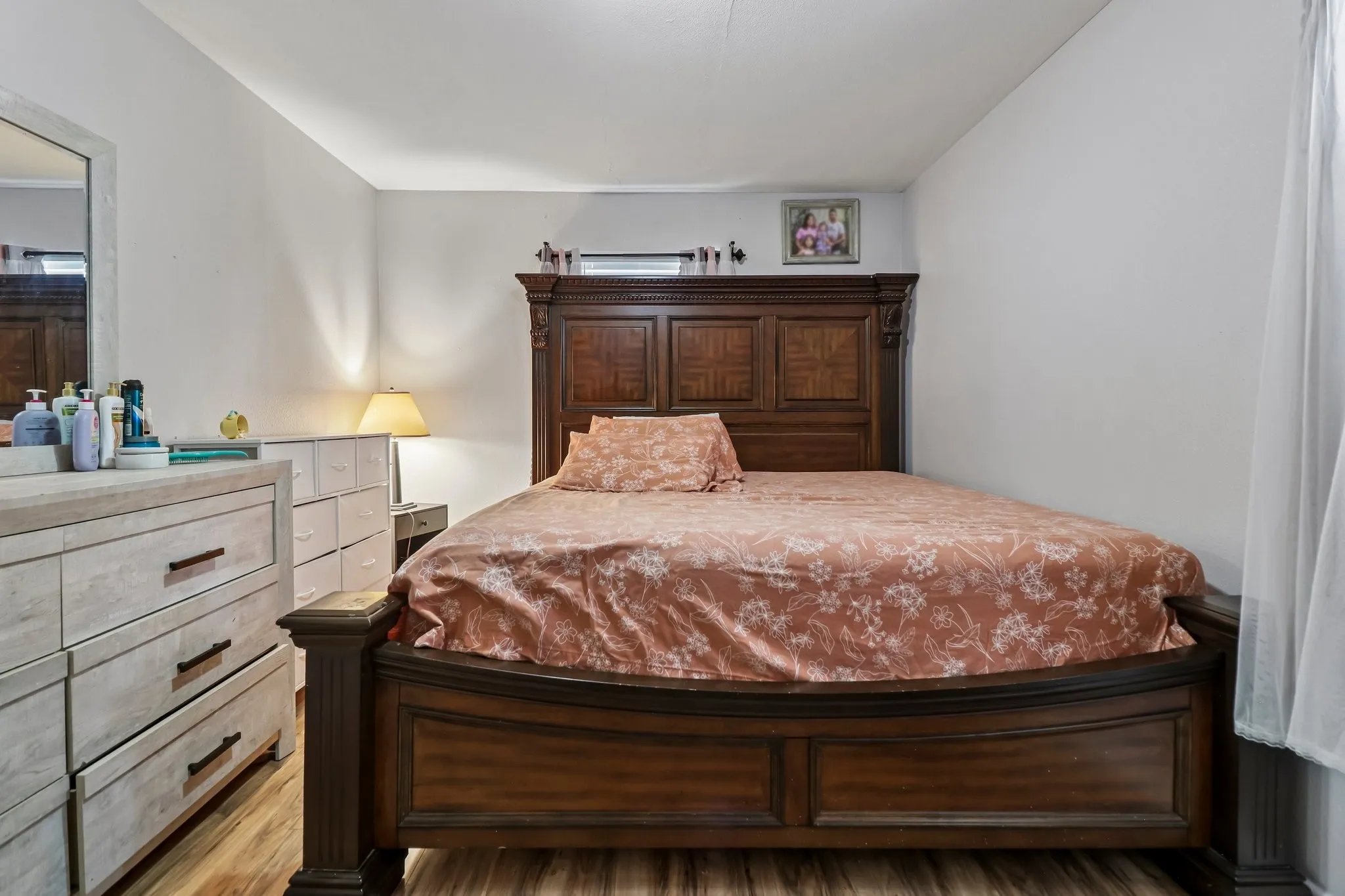 Wood-finish flooring with white walls and a large window with sheer drapes