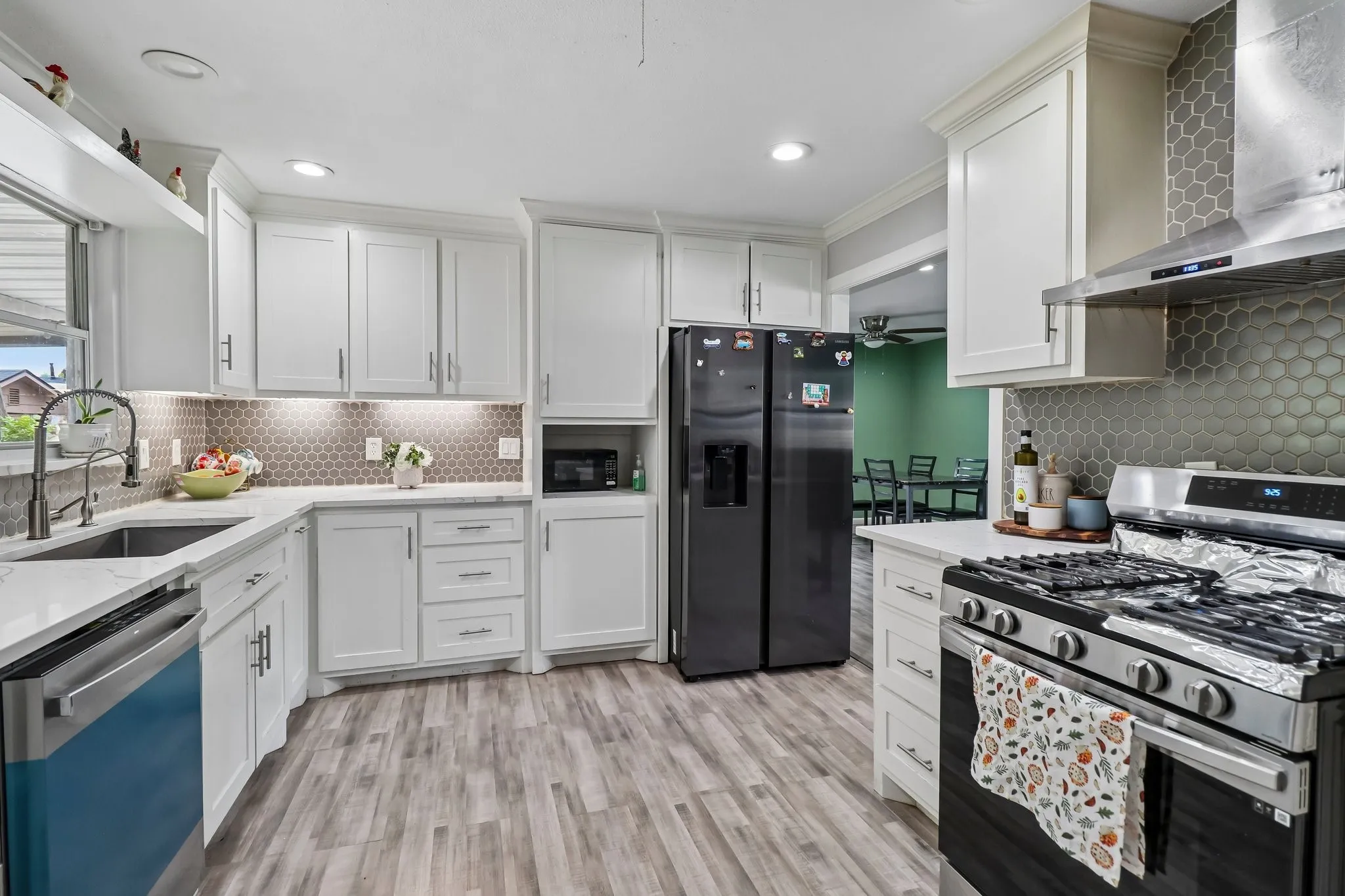 White shaker cabinetry, quartz countertops, hexagonal tile backsplash, stainless steel appliances, and wood-finish flooring