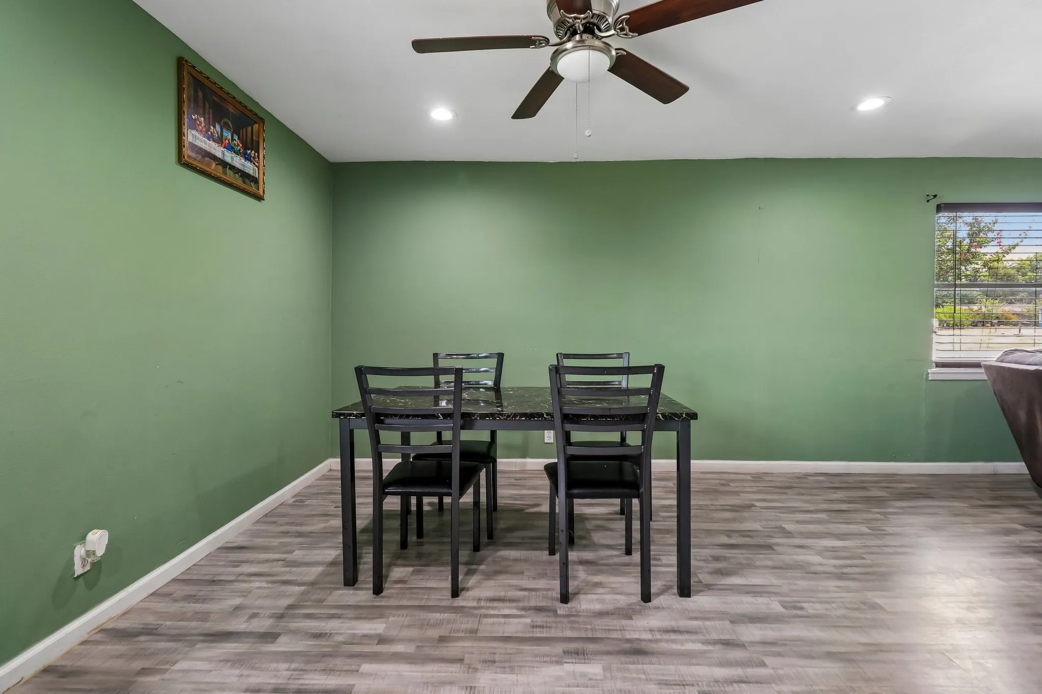 Bright dining area featuring crisp sage-green walls, wood-finish plank flooring, and ceiling fan with integrated lighting