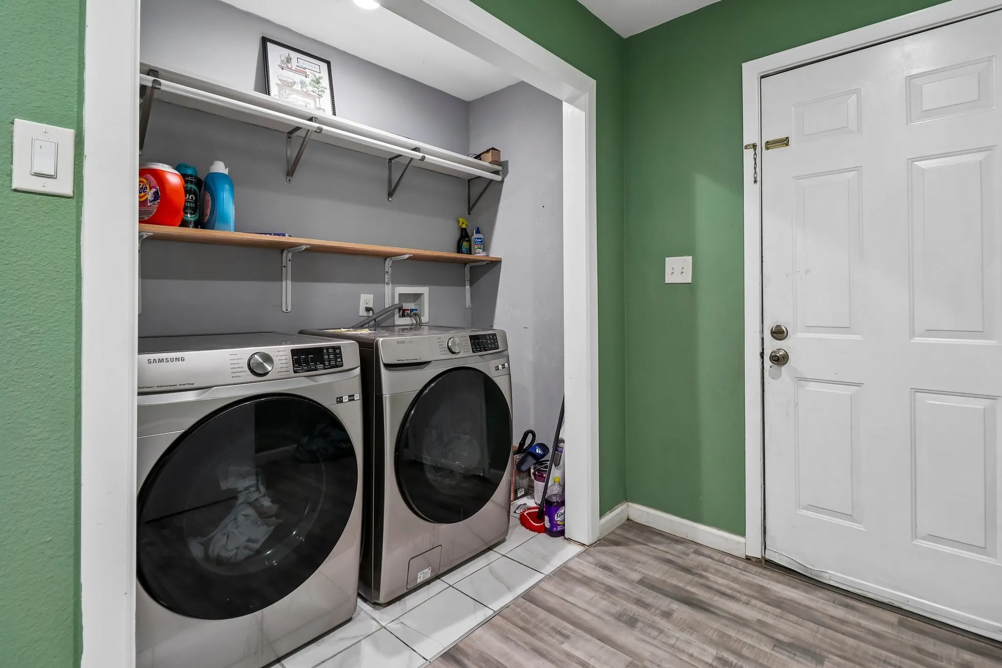 Dedicated laundry area featuring wood-finish flooring, white tile, and built-in shelving