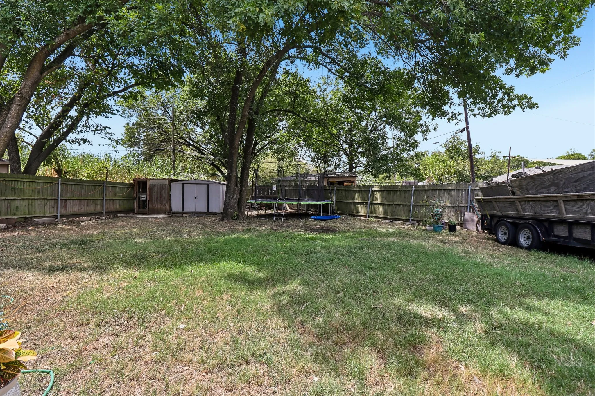 Expansive outdoor space featuring a wood fence, mature trees, and a storage shed