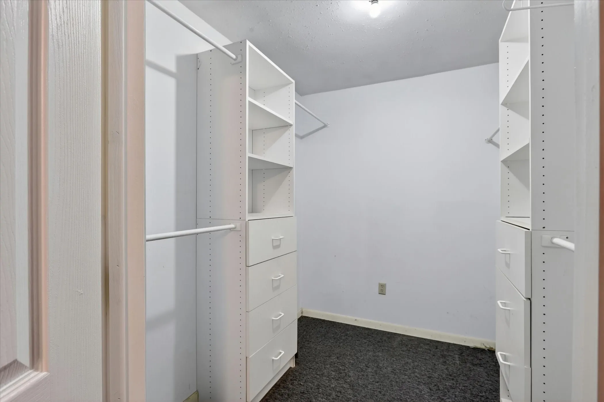 Walk-in closet featuring built-in shelving units, integrated drawers, white hanging rods, and dark carpet flooring