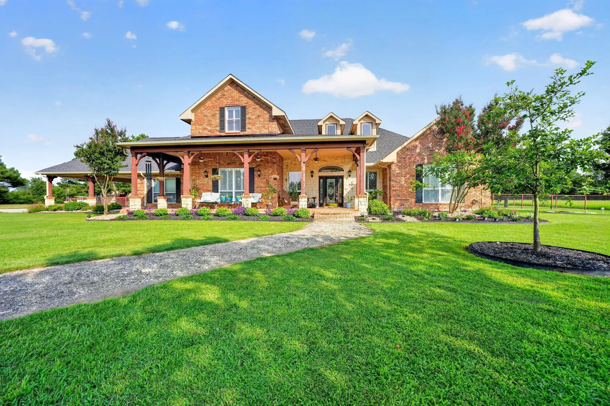 Brick and stone exterior featuring a covered front porch with timber columns, dormer windows, and a black shingle roof
