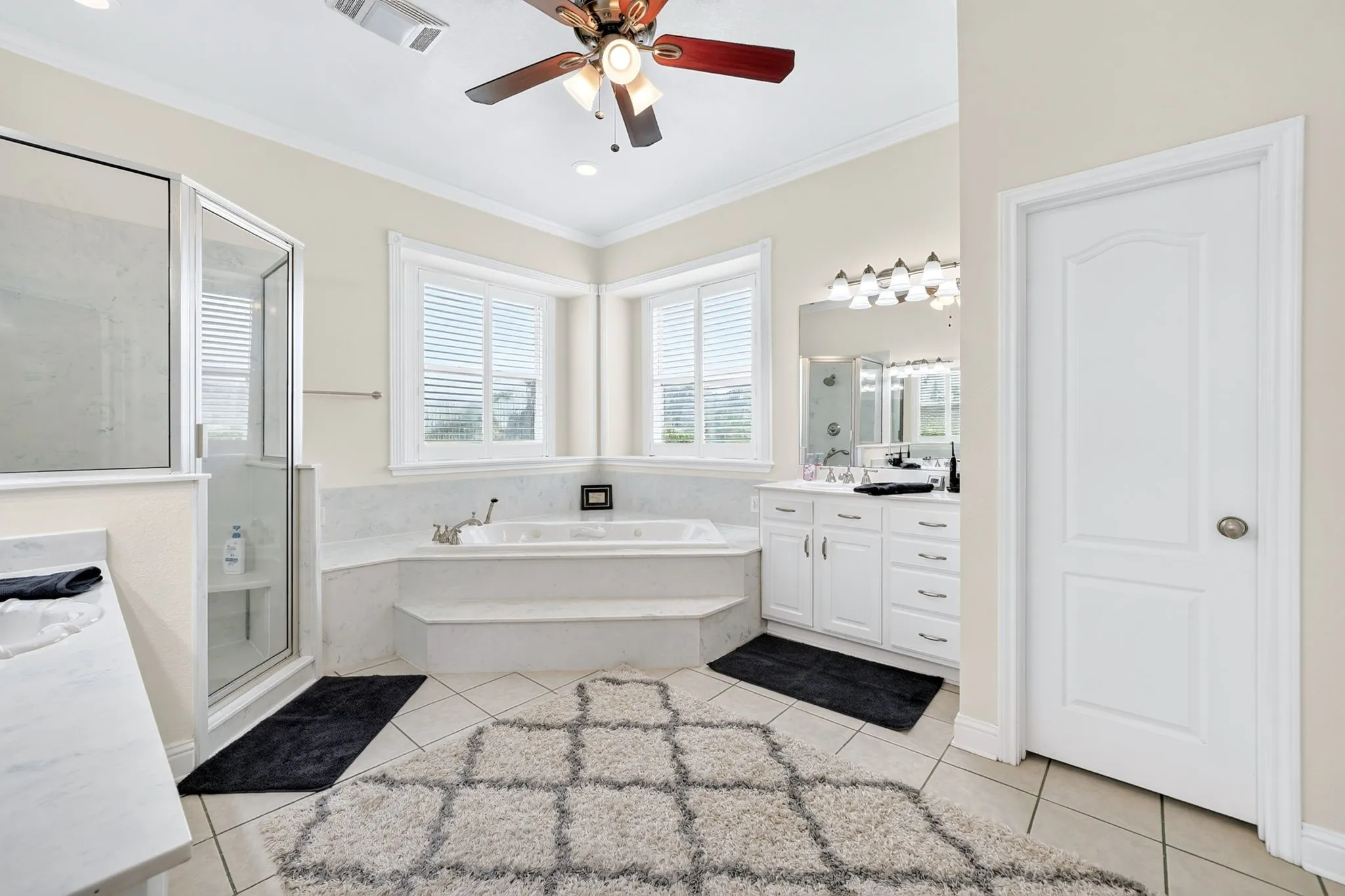 Bathroom featuring a corner soaking tub with steps, dual vanity with white cabinetry, glass-enclosed shower, and tiled flooring