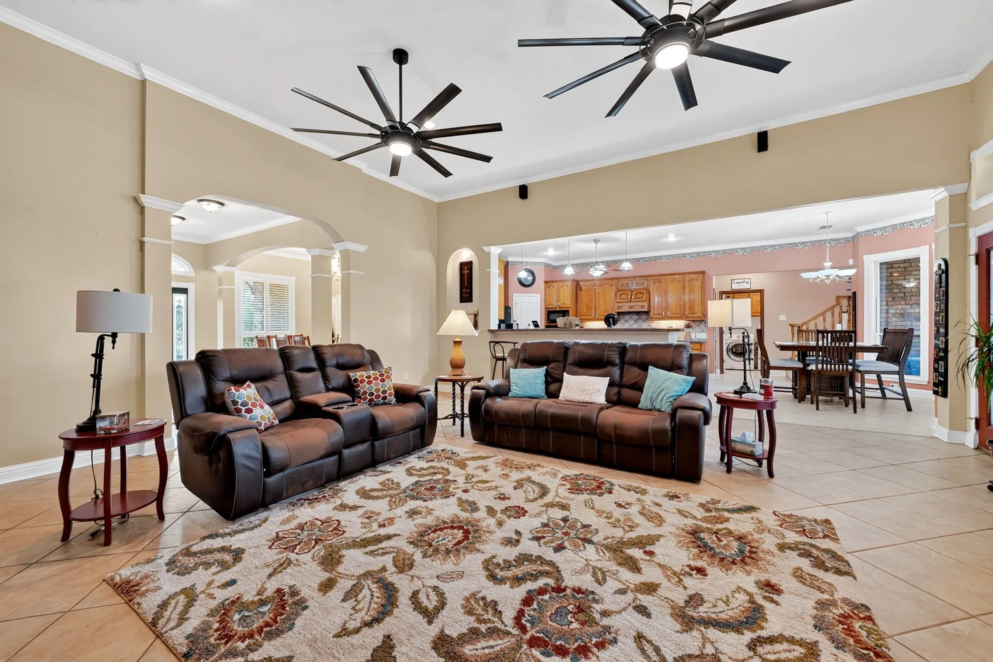 Spacious living area featuring tile flooring, crown molding, and two ceiling fans