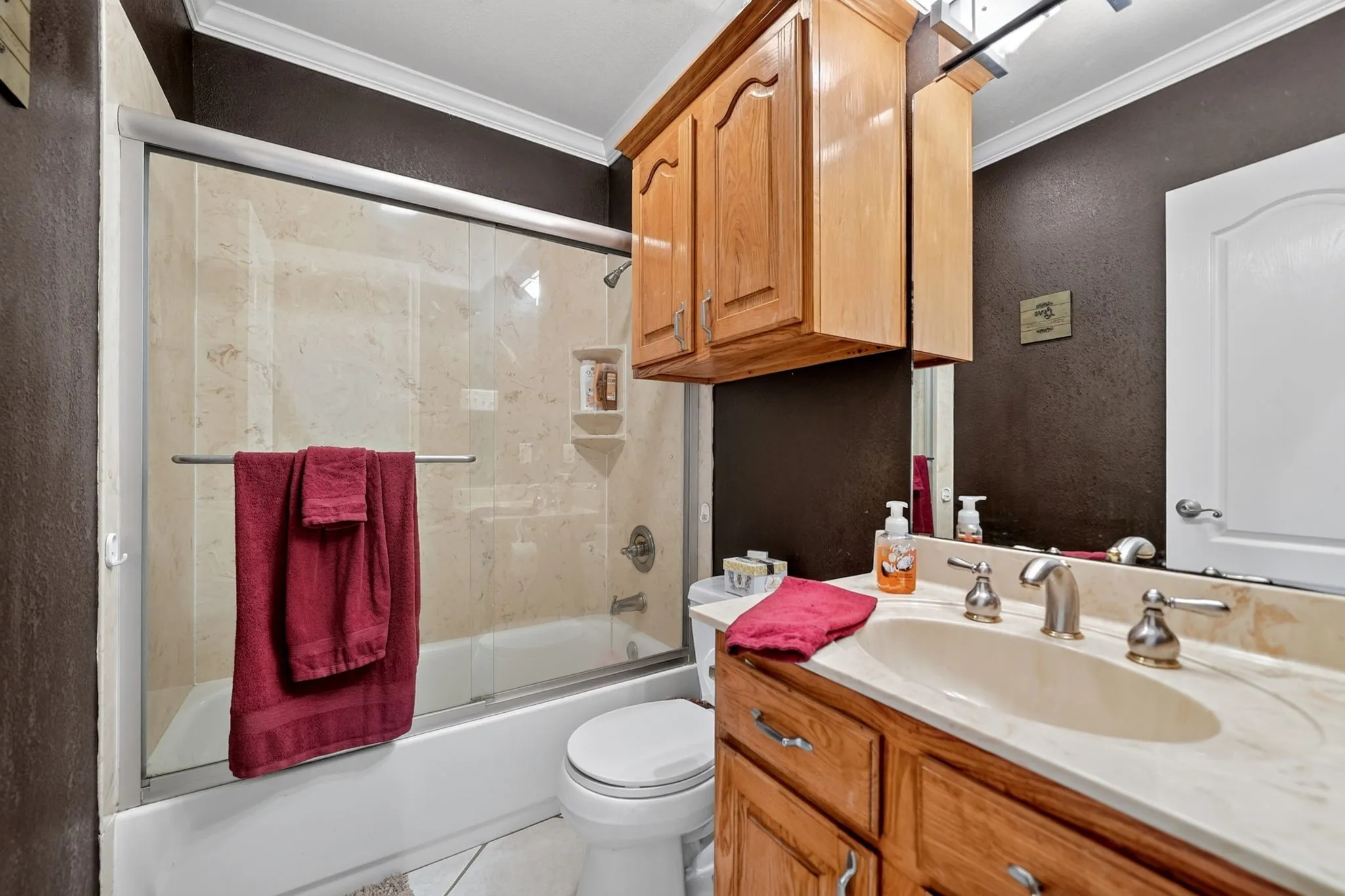 Bathroom featuring a built-in vanity with wood cabinetry and a light-toned countertop, an integrated sink with a brushed nickel faucet, a mirror with overhead lighting, and an adjacent shower-tub combination with a sliding glass door and tiled surround