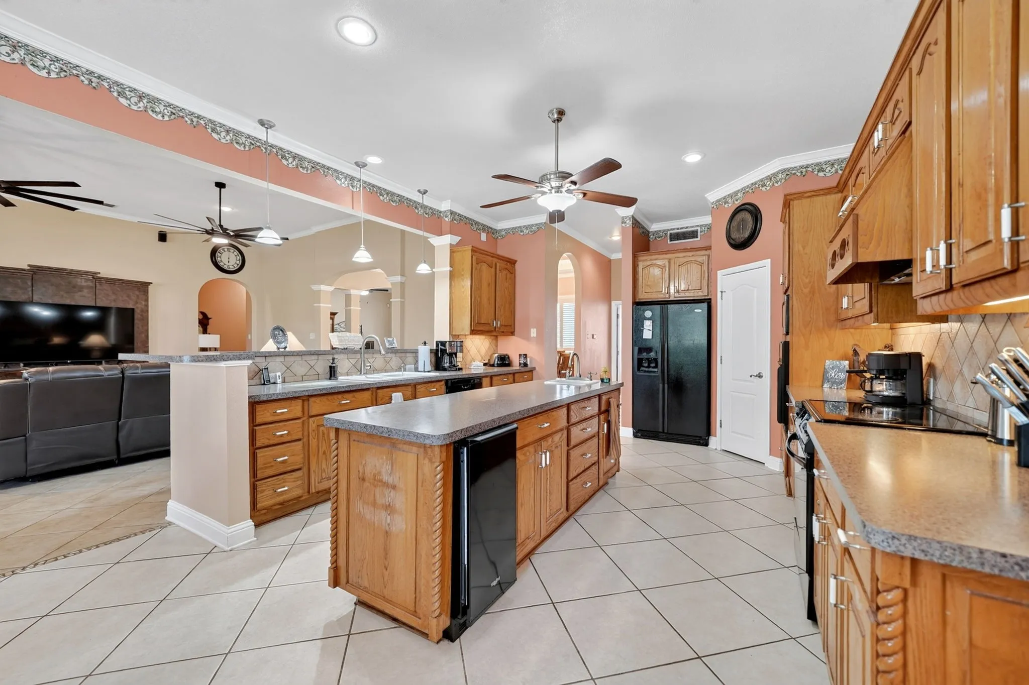Expansive kitchen featuring a central island with storage, tile flooring, wood cabinetry, a built-in electric cooktop, and a black French door refrigerator