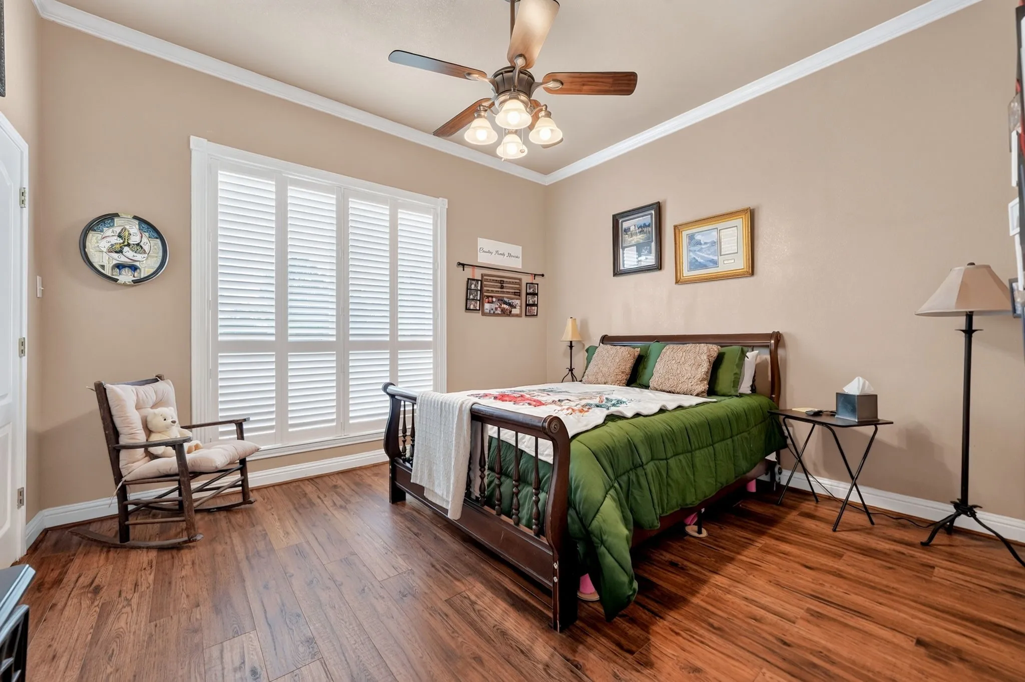 Bedroom featuring expansive windows with white plantation shutters, rich wood-finish flooring, and a ceiling fan with integrated lighting