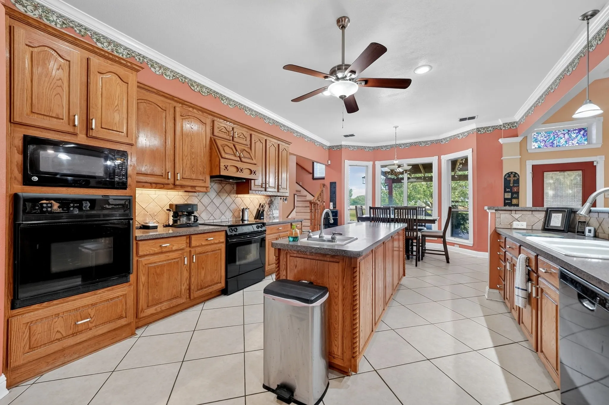 Kitchen featuring oak cabinetry, integrated double oven, center island with sink, tile flooring, and a bay window dining area