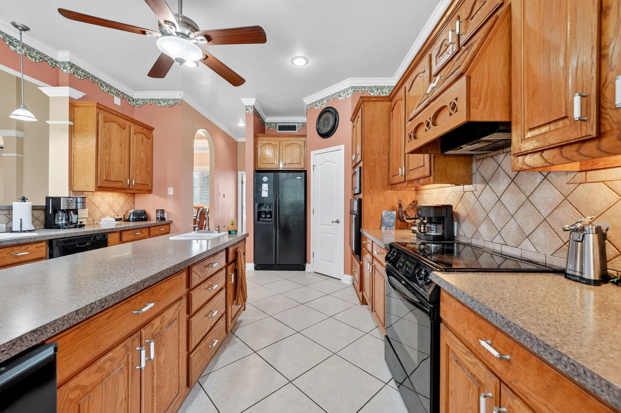Spacious kitchen featuring extensive wood cabinetry, stone-finish countertops, and a full suite of black built-in appliances including a refrigerator and range