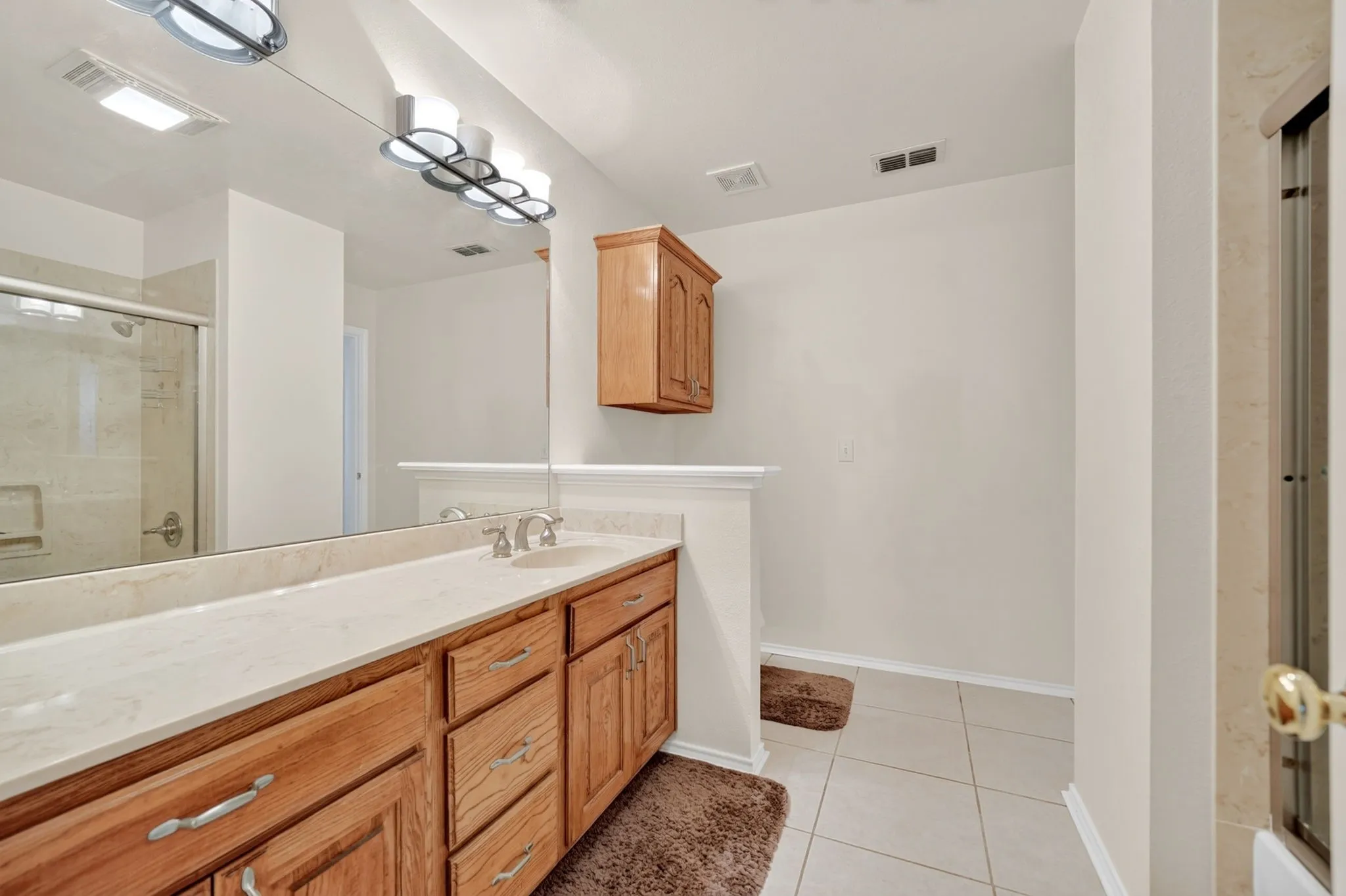 Bathroom featuring a double vanity with light wood cabinetry, a light-colored countertop, and an expansive mirror