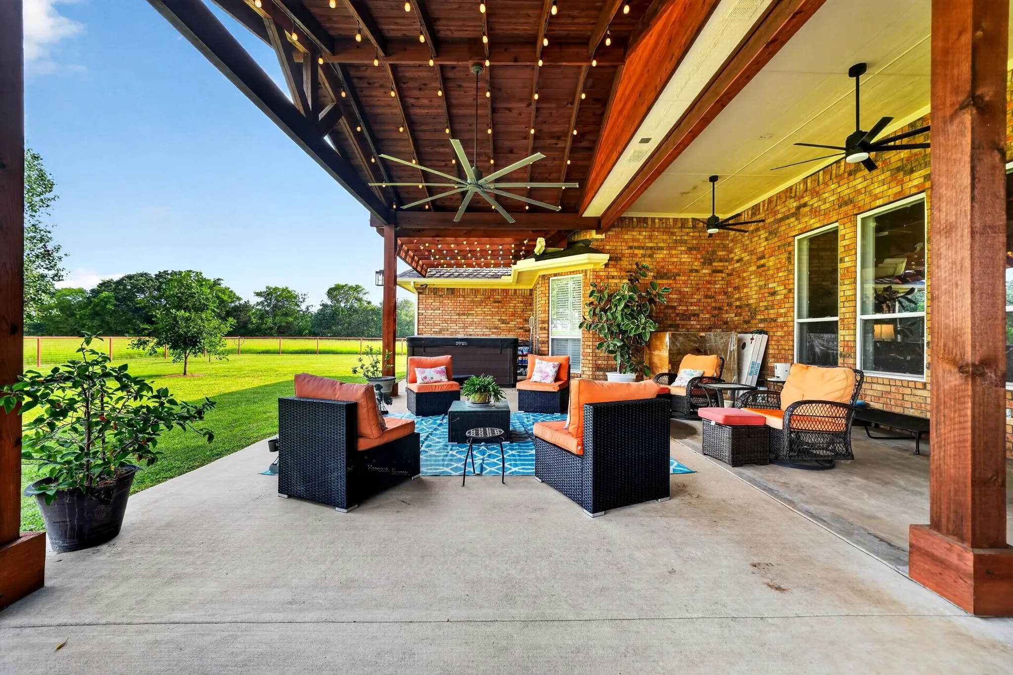 Expansive covered patio featuring a wood-plank ceiling with exposed beams, string lighting, and multiple ceiling fans