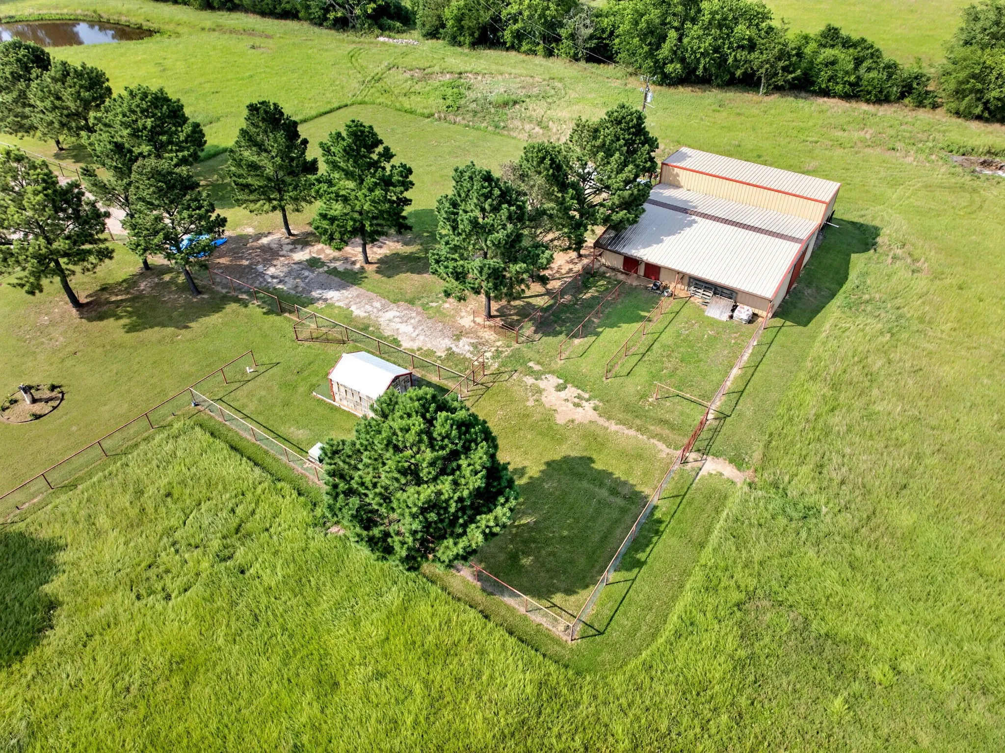 Expansive rural property featuring a large outbuilding with a metal roof, multiple fenced enclosures, and a natural pond