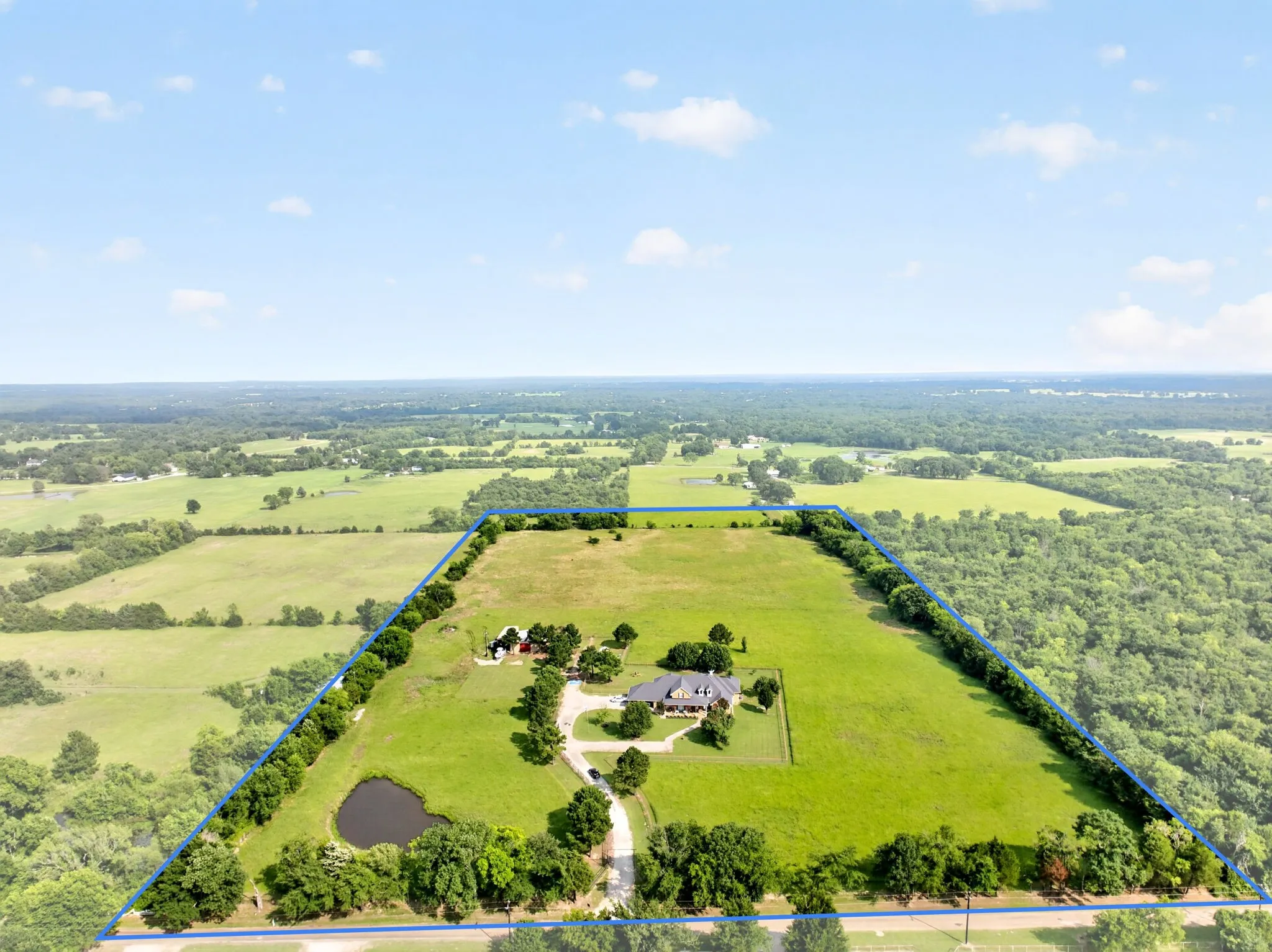 Expansive acreage featuring a main residence, secondary structure, private pond, and mature tree lines