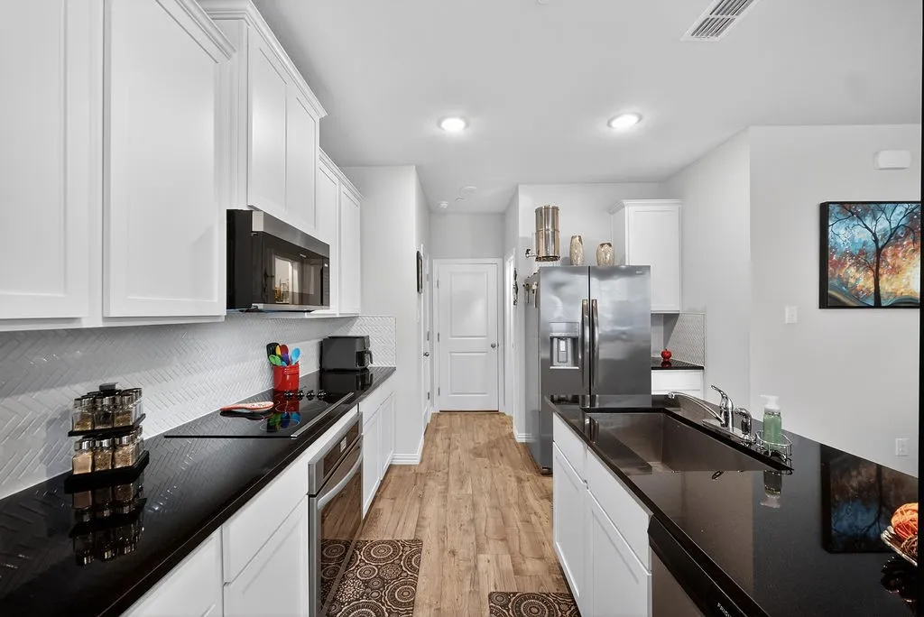 Modern kitchen featuring white shaker cabinetry, dark countertops, wood-finish flooring, a stainless steel refrigerator, and an integrated stainless steel oven with a built-in microwave