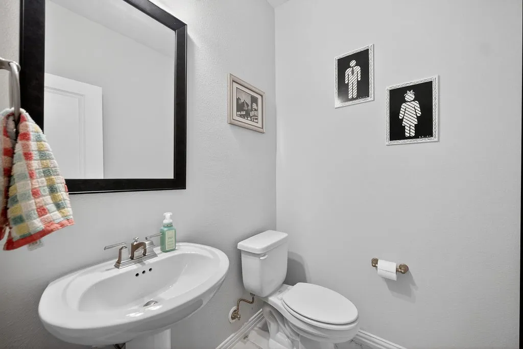Pedestal sink with a polished chrome faucet set beneath a rectangular mirror with a dark frame