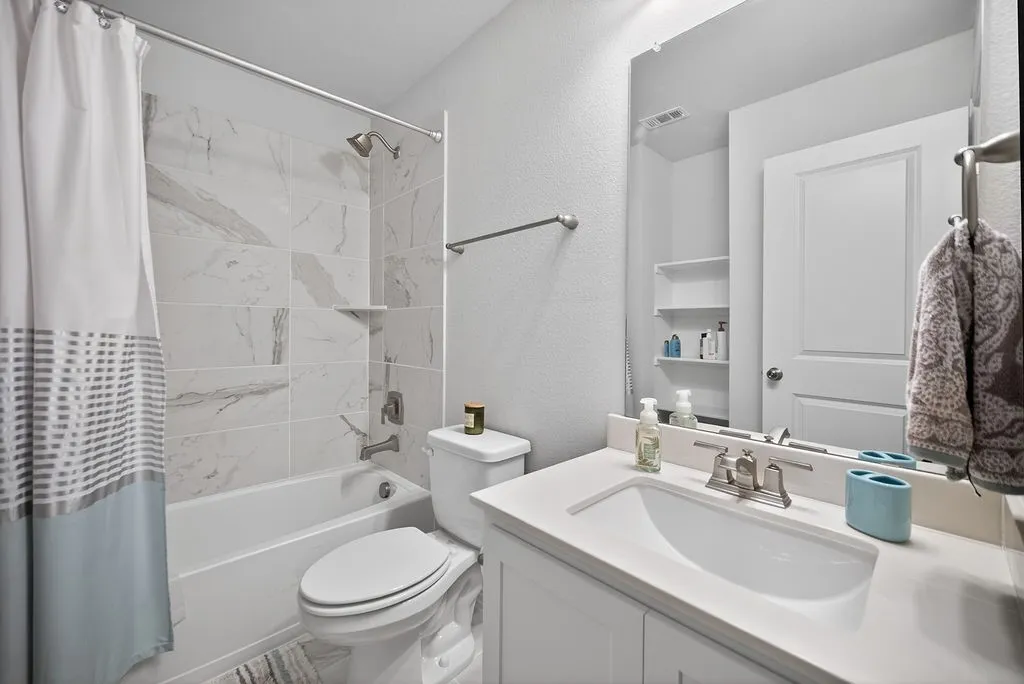 Bathroom featuring white subway tile shower surround with a built-in shelf, white porcelain tub, toilet, and a vanity with an integrated sink and light-colored countertop
