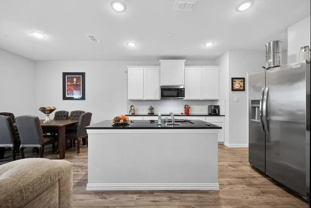 Kitchen featuring white cabinetry, black countertops, stainless steel appliances, and wood-finish flooring