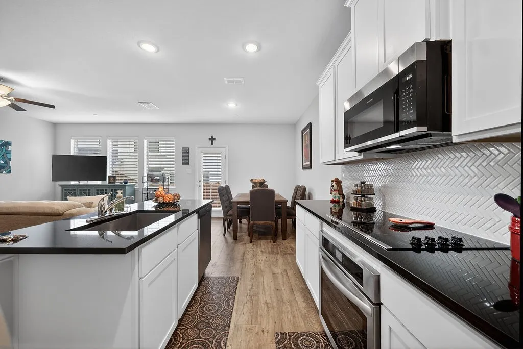 Kitchen featuring white cabinetry, black countertops, stainless steel appliances, herringbone tile backsplash, and wood-finish flooring